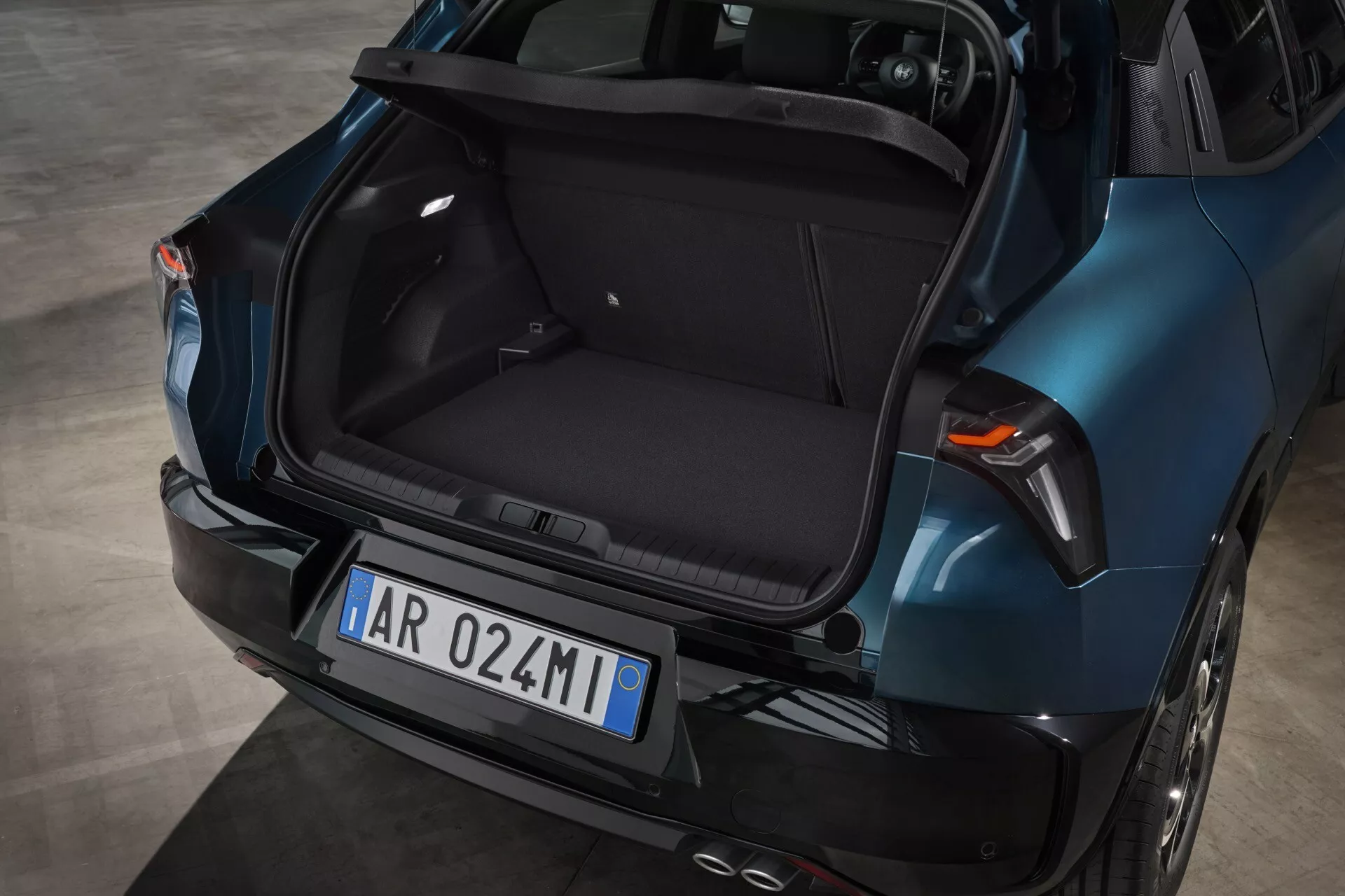 Zadný pohľad na Alfa Romeo Junior 2024 ukazujúci prázdny priestor kufra, metalickú modrú farbu, moderný dizajn s aerodynamickými líniami, integrované brzdové svetlá na zadnej klapke, LED zadné svetlá a dvojitý výfukový systém.