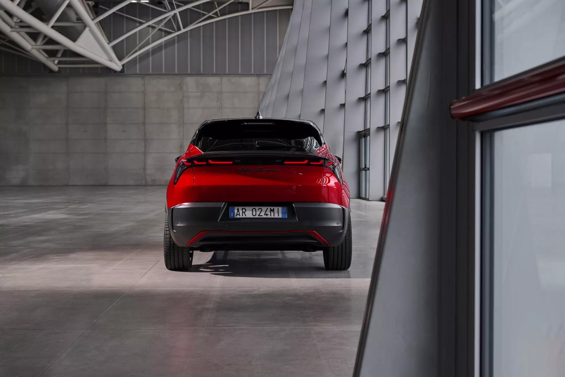 Zadný pohľad na Alfa Romeo Junior 2024 predstavujúci dizajnové prvky a LED zadné svetlá v priemyselnom prostredí s leštenou podlahou a ambientným osvetlením