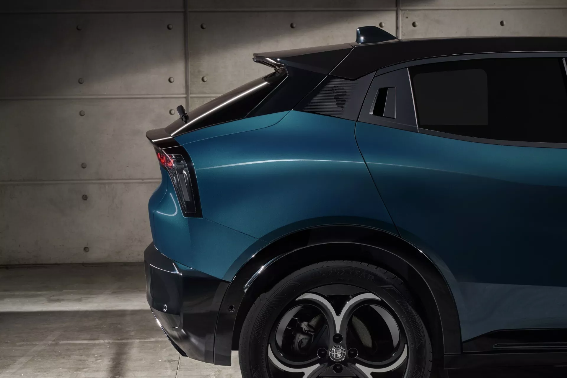 Alfa Romeo Junior (966) ročník 2024 predvádzajúci zadný blatník s LED zadným svetlom, dizajnom kolesa s viacerými špicami a metalickým modrým lakováním, čo naznačuje moderný styling a možno elektrické alebo hybridné schopnosti.