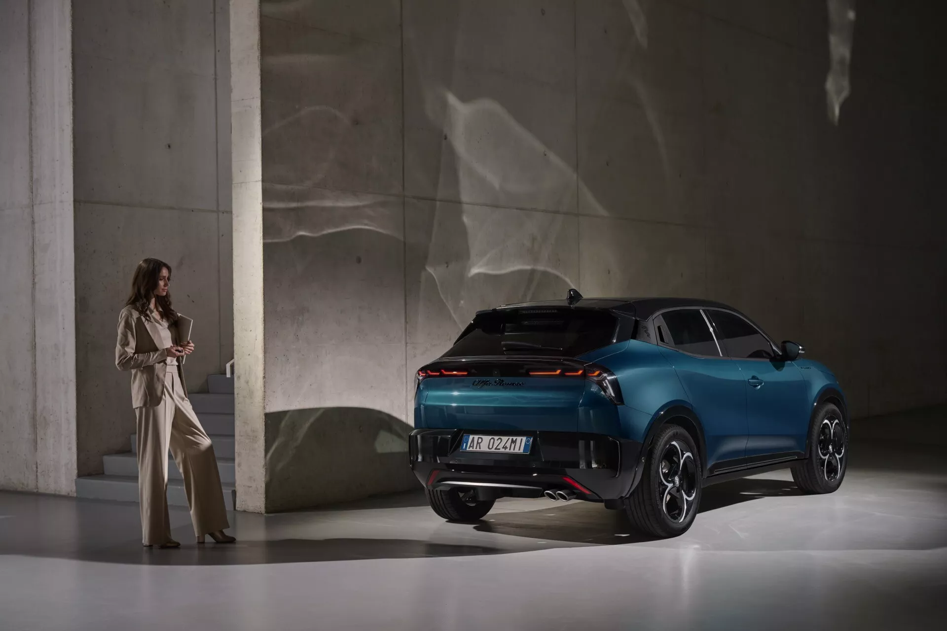 Alfa Romeo Junior 2024 fotografované z trojštvrtovej zadnej pohľadu v štúdiu, zobrazujúce LED zadné svetlá, športový zadný nárazník, zliatinové kolesá s viacerými ramenami, metalickú modrú farbu a líniu strechy ako kupé medzi inými funkciami