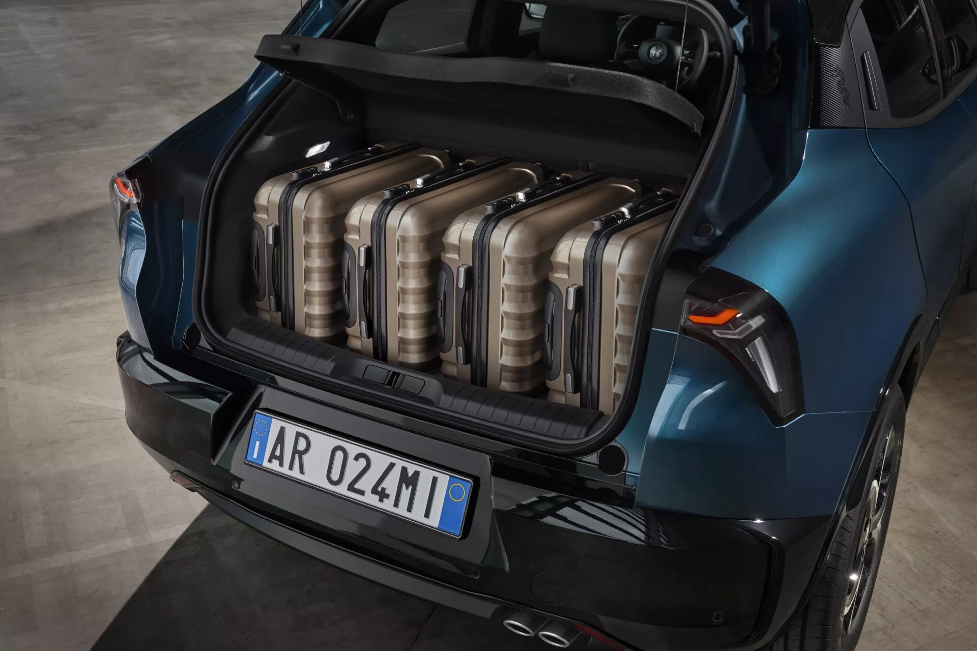 Alfa-Romeo Junior 966 z roku 2024 predstavuje svoj priestranný modrý kufor z vysokého uhla, ukazuje usporiadanie batožiny a dizajnové prvky vrátane tvaru zadných svetiel a zakrivenia zadného nárazníka.