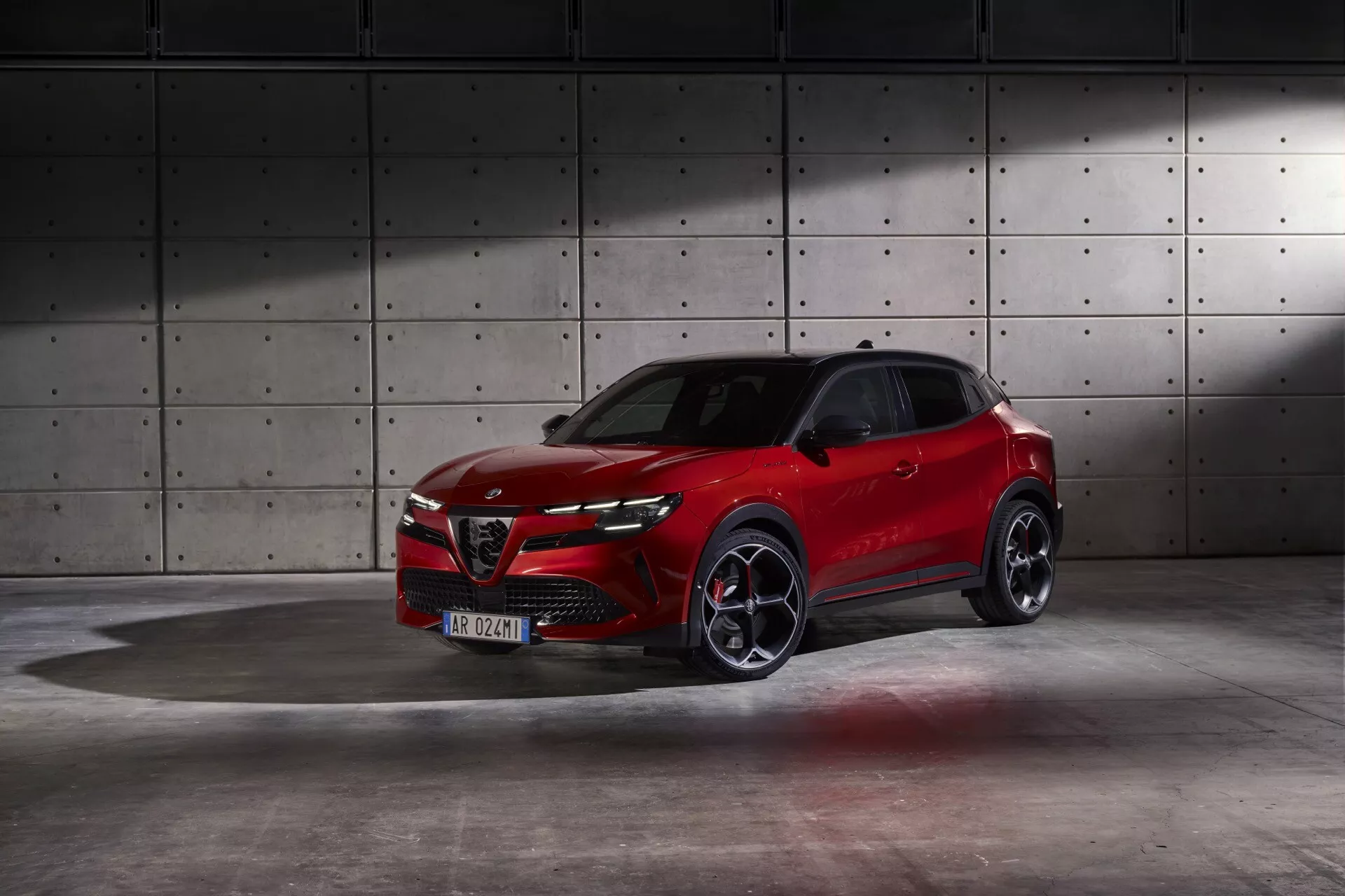 Alfa Romeo Junior 966 ročník 2024 vo výraznej červenej farbe predvádzajúca dynamický dizajn a pokročilé funkcie v profesionálnom štúdiu s priemyselným pozadím