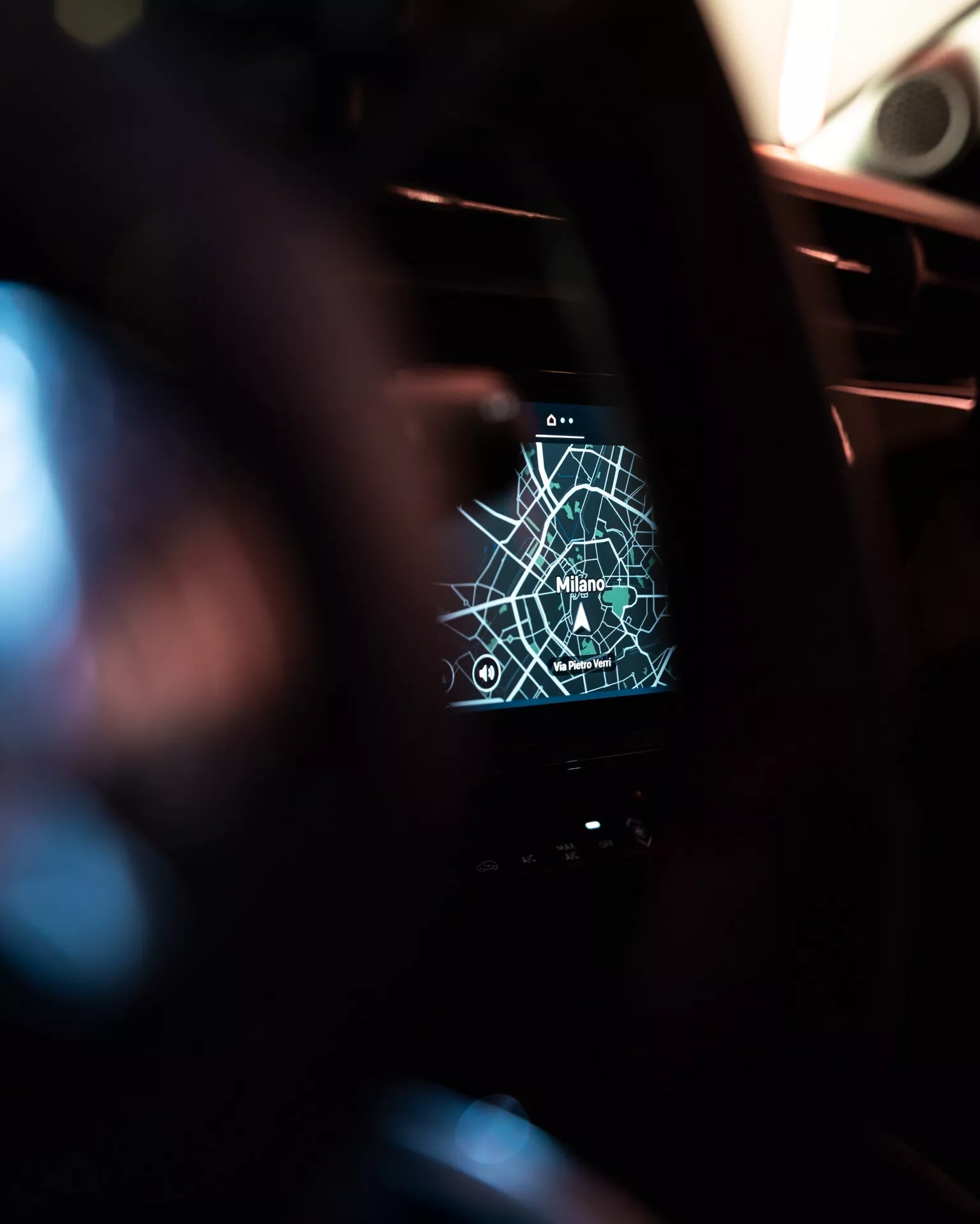 Interiérový pohľad na Alfa Romeo Junior 2024 zameraný na systém infotainment zobrazujúci GPS mapu Milána s navigačnými ikonami, z pohľadu vodiča s malou hĺbkou ostrosti