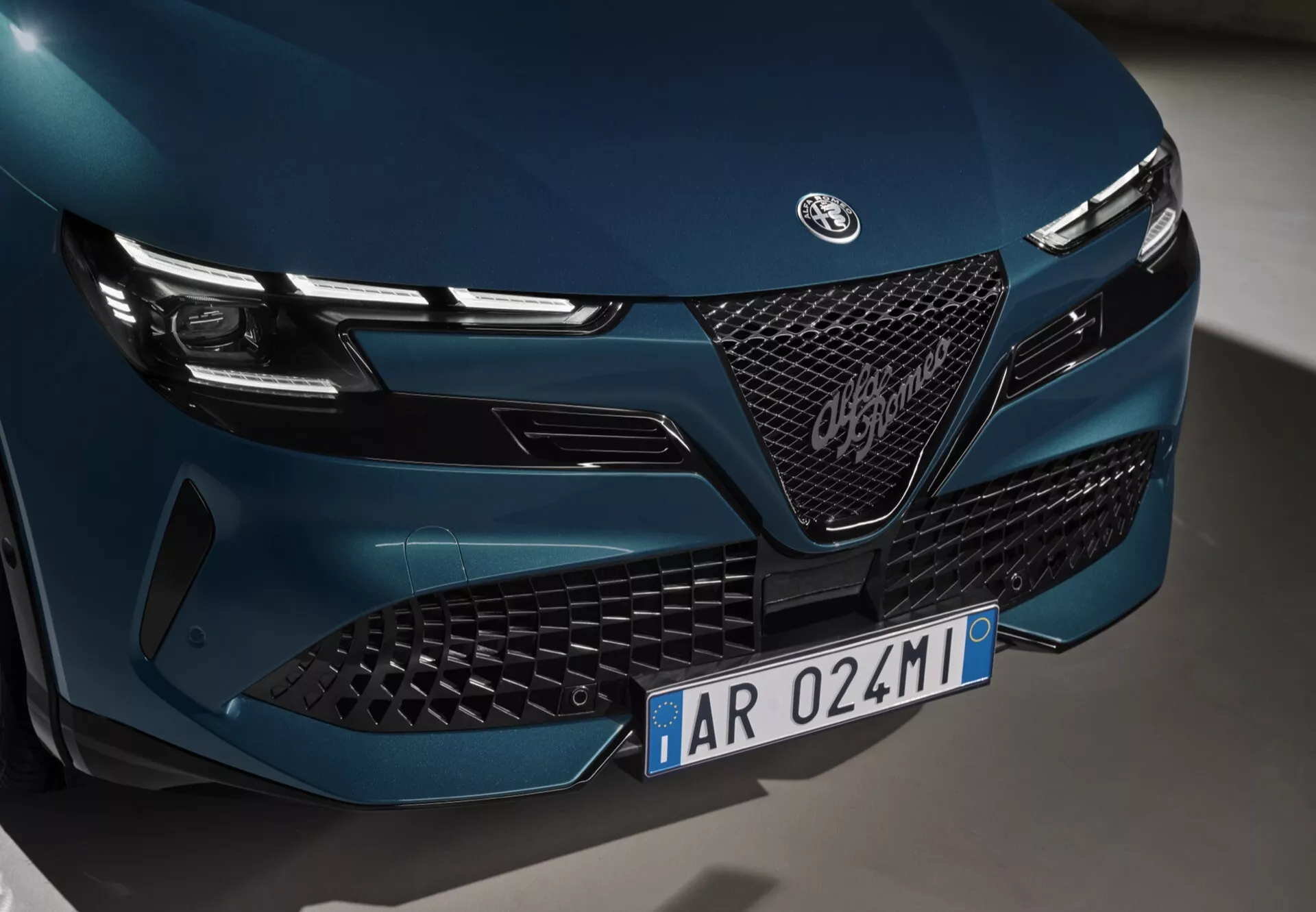 Detailný pohľad na prednú časť Alfa-Romeo Junior 2024 s dôrazom na mriežku, emblém a LED svetlomety s elegantným a agresívnym dizajnom, záber z nízkeho uhla z ľavej strany