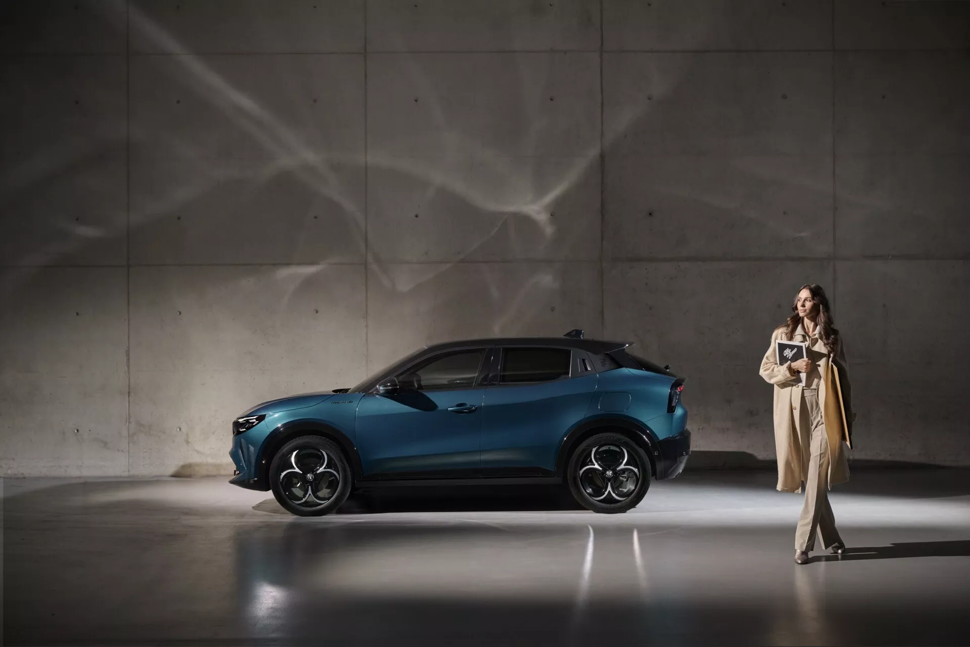 Dynamický bočný pohľad na Alfa Romeo Junior 966 2024 v metalickej modrej, zdôrazňujúci jeho elegantný dizajn a pokročilé vlastnosti vrátane športových zliatinových kolies a aerodynamického profilu, v sofistikovanom interiéri s dramatickým osvetlením