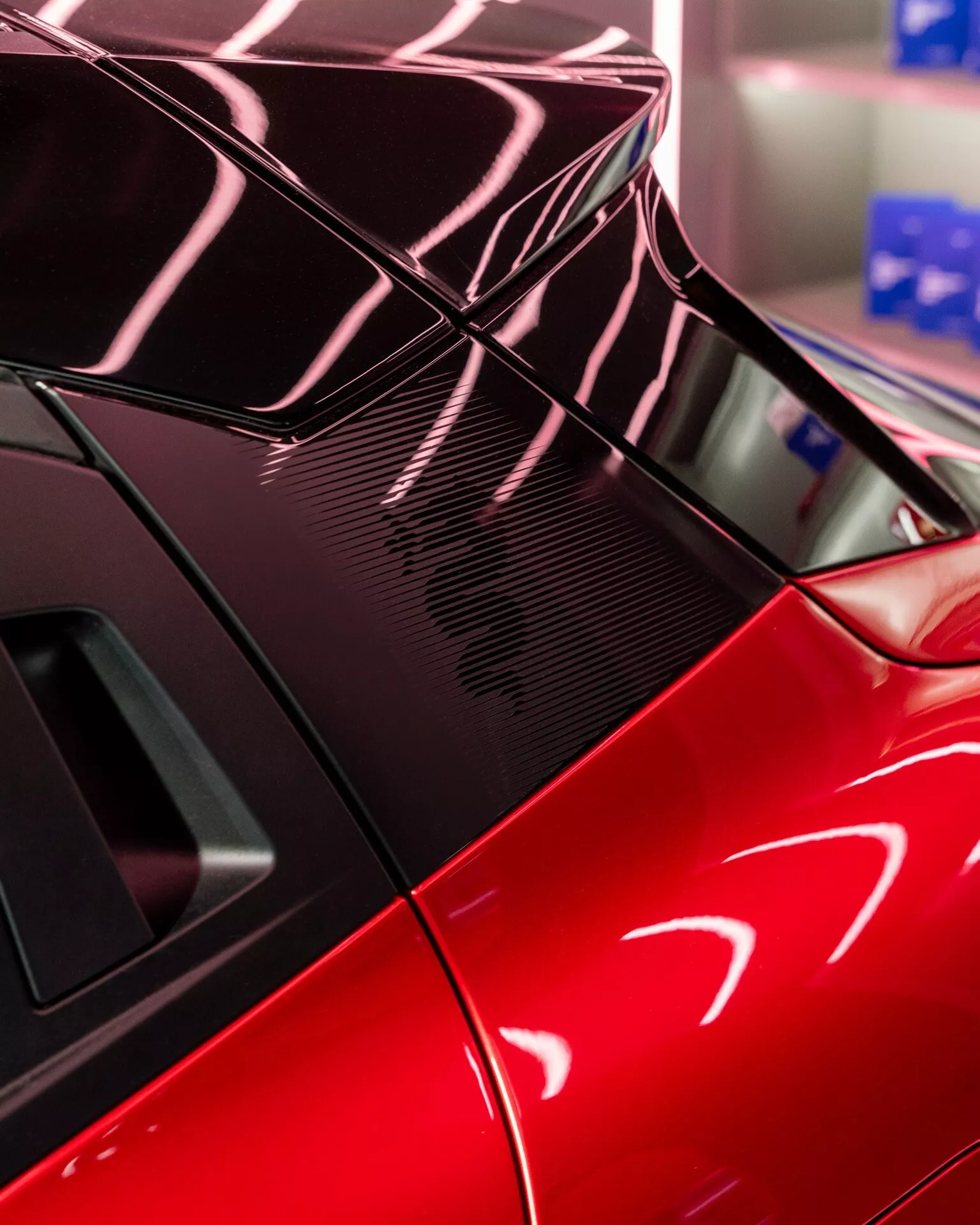 Detailný pohľad na zadnú časť Alfa-Romeo Junior 2024 s športovým červeným prevedením, integrovaným spoilerom, detailmi z uhlíkových vlákien a dizajnom zadného okna odrážajúcim zložité svetelné vzory.