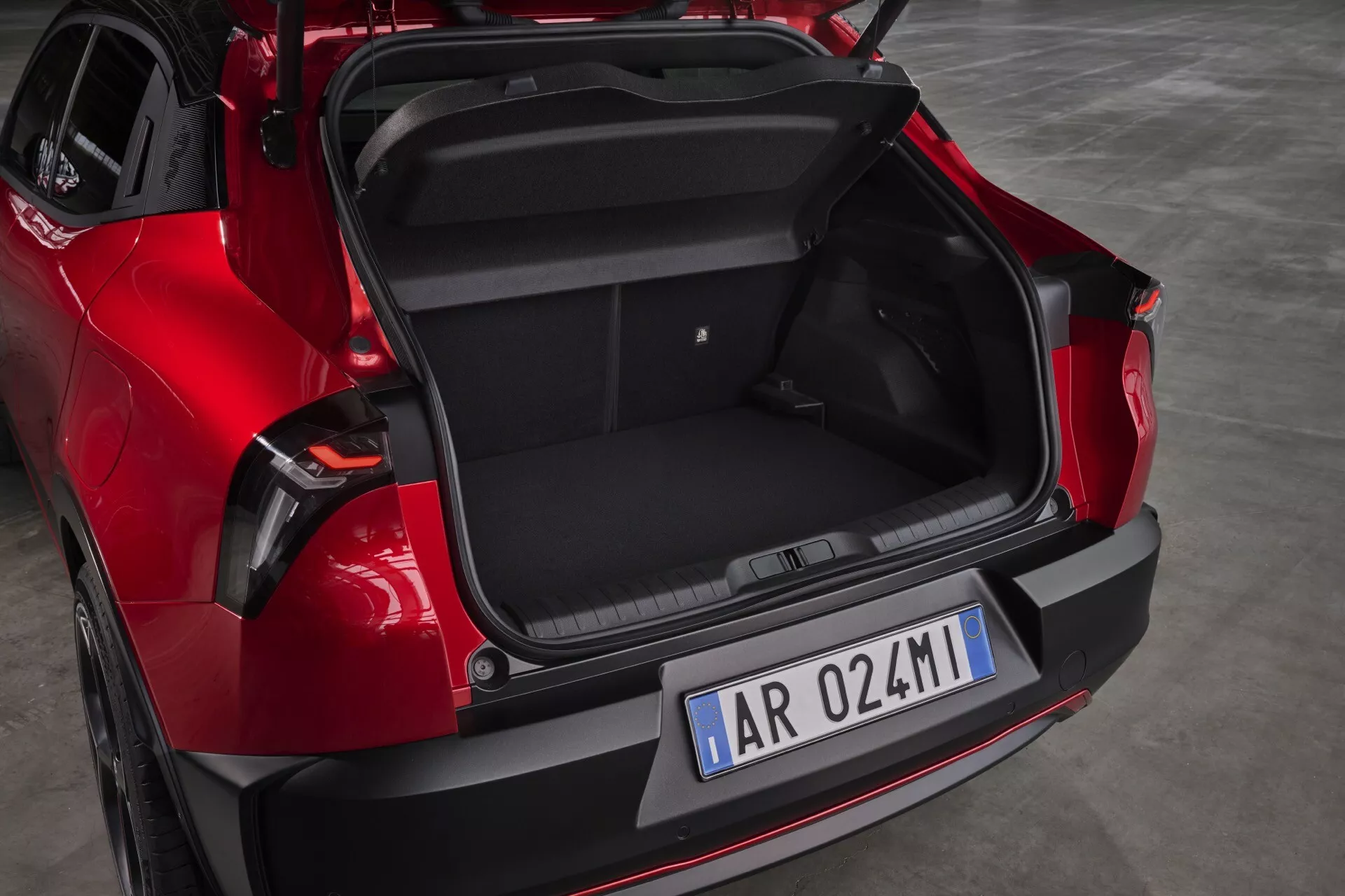 Zadný pohľad na červené Alfa-Romeo Junior 966 z roku 2024, ktorý ukazuje kapacitu batožinového priestoru a moderné dizajnové prvky ako automatickú výklopnú dvere, čiernu vložku nárazníka pre ochranu proti škrabancům a parkovaciu technológiu a štýlové LED zadné svetlá.