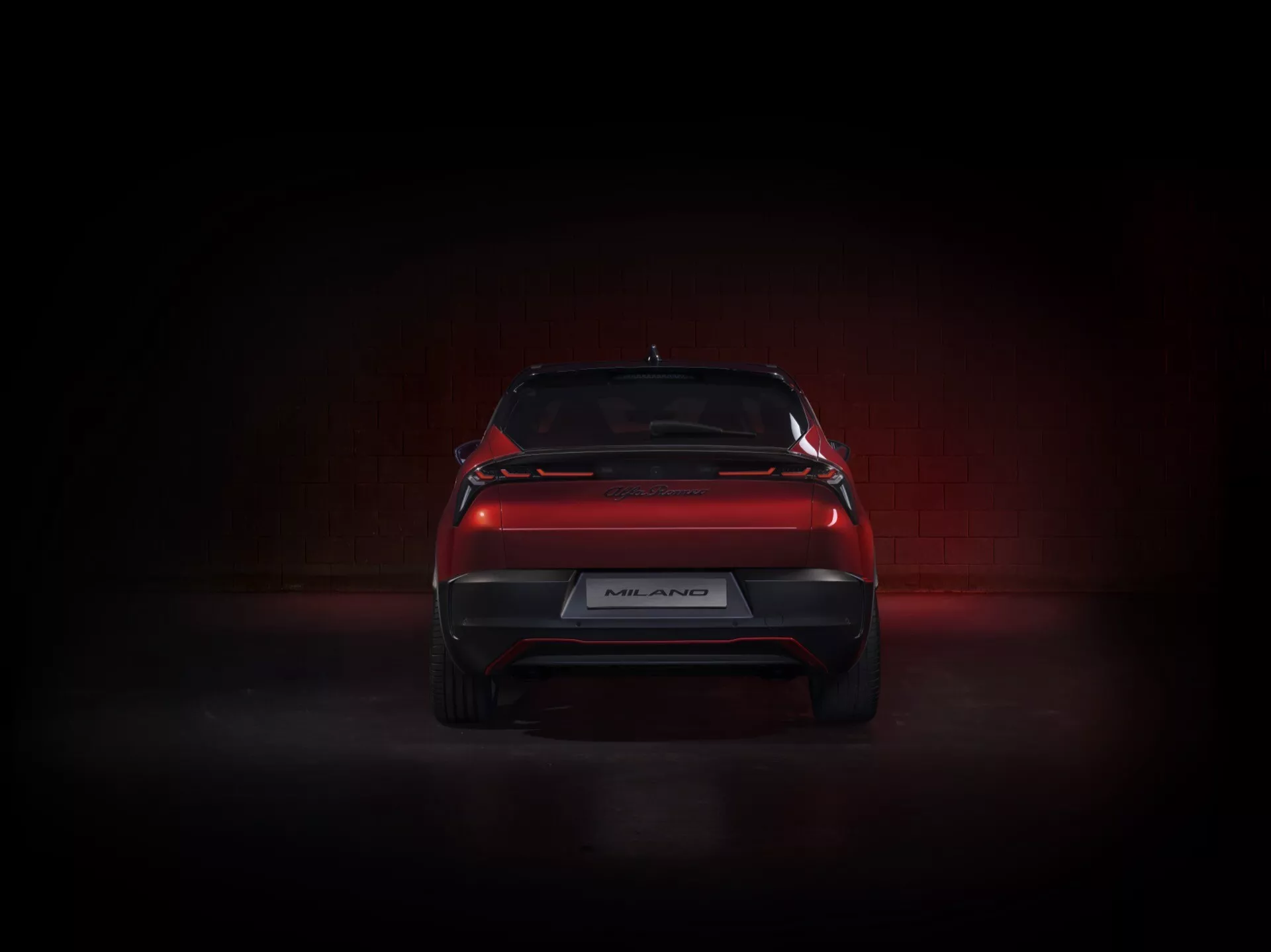 Zadný pohľad na Alfa Romeo Junior 2024 prezentujúci elegantný dizajn s LED zadnými svetlami, športovým zadným difúzorom a spoilerm na veku batožinového priestoru v dramatickom osvetlení štúdia