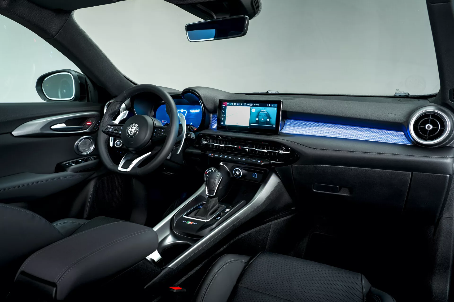 Interiérový pohľad na stranu spolujazdca Alfa Romeo Tonale 2022, zdôrazňujúci multifunkčný volant, digitálny palubnú dosku, radiacu páku automatickej prevodovky s koženou manžetou, volič režimu jazdy, infotainment systém s obrazovkou, ambientné osvetlenie a prémiové kožené sedadlá s kontrastným prešívaním.