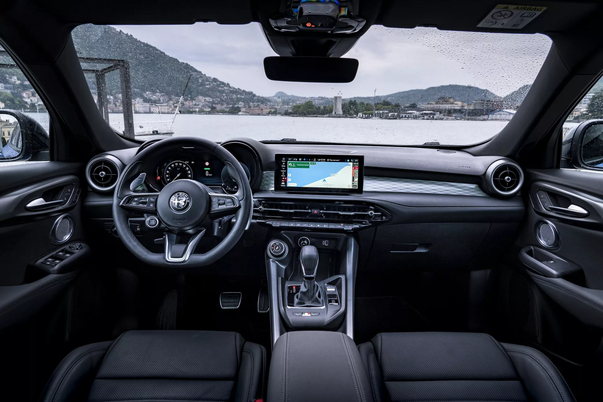 Interiérový pohľad na Alfa Romeo Tonale 2022 zobrazujúci palubnú dosku, volant, prednú časť kabíny, digitálny displej s navigáciou, stredovú konzolu a čalúnené predné sedadlá z perspektívy zadných sedadiel