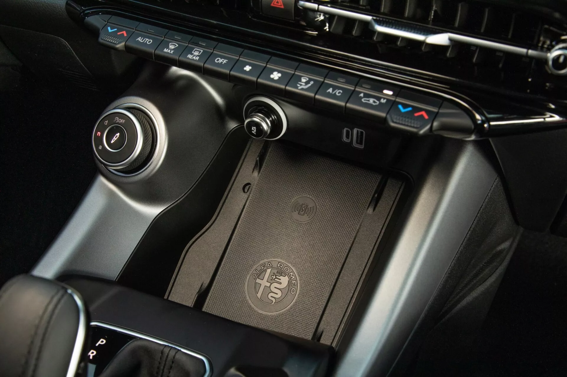 Detailný pohľad na centrálnu konzolu Alfa Romeo Tonale 2022, zobrazuje panel klimatizácie, bezdrôtovú nabíjaciu podložku, radiacu páku a ovládací kotúč infotainmentu s prémiovým prevedením a moderným dizajnom.