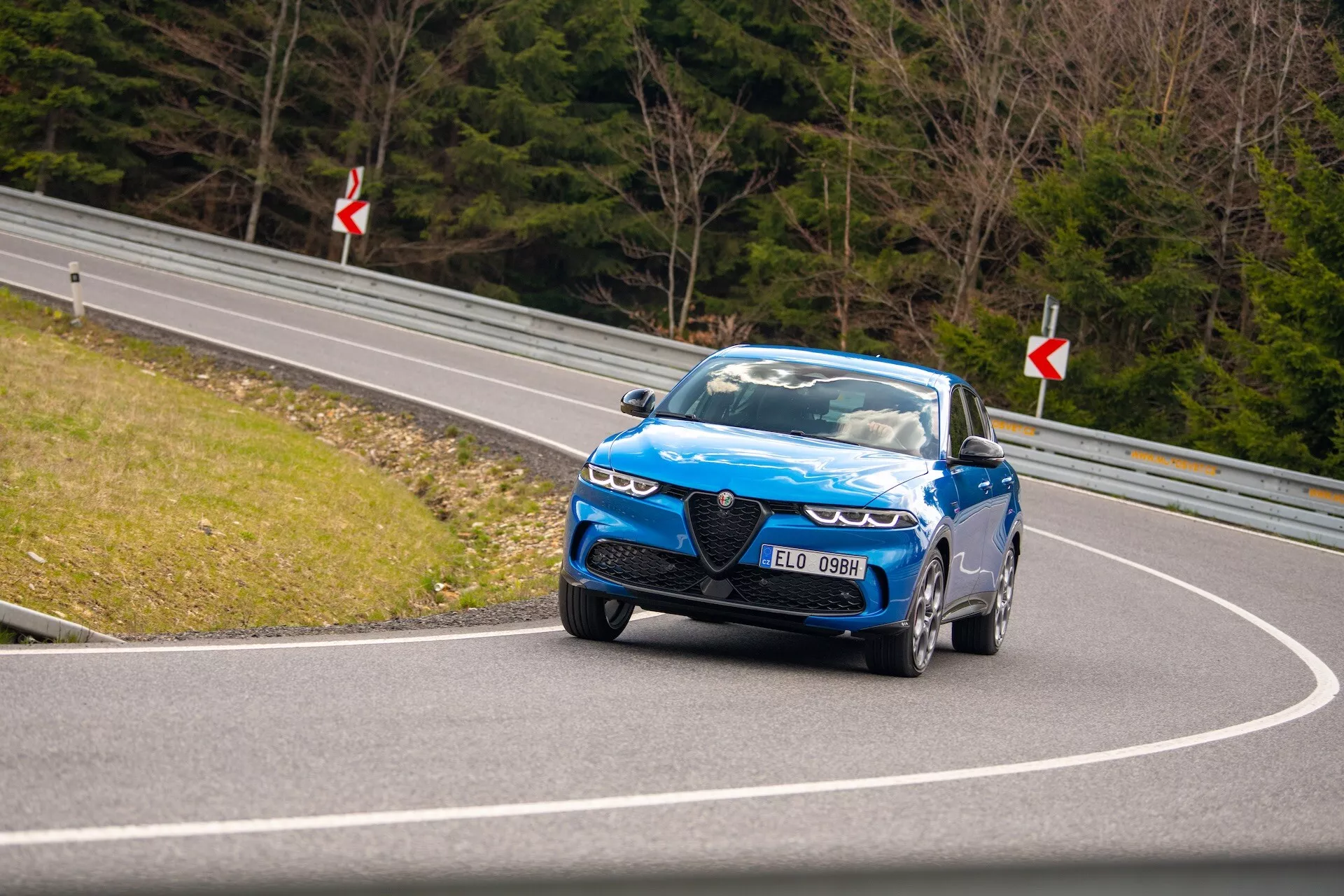 Dynamická jazda Alfa Romeo Tonale 2022 po zákrutej ceste s pohľadom na prednú štvrtinu, LED svetlomety, charakteristickú mriežku a výkonné kolesá
