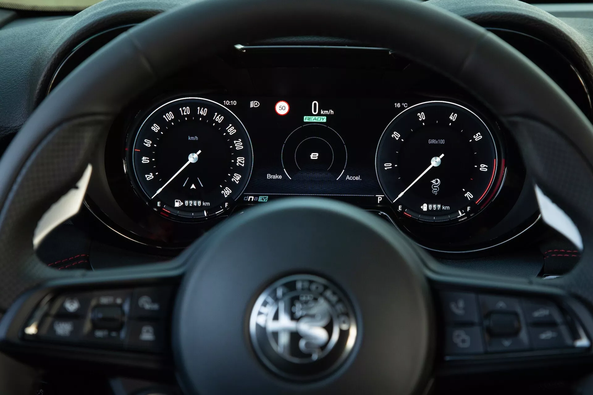 Interiér Alfa Romeo Tonale 2022 zobrazujúci pohľad vodiča na trojramenný multifunkčný volant a prístrojovú dosku s analógovými ukazovateľmi a centrálnym digitálnym displejom ukazujúcim nulovú rýchlosť a otáčky, funkcie pre spojenie a asistenčné systémy vodiča