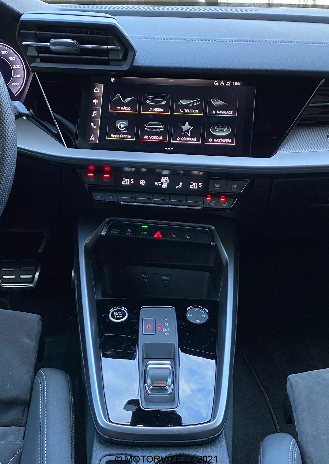 Interiér Audi A3 2020 Sportback s výhľadom na stredovú konzolu a prístrojovú dosku, zdôrazňujúci funkcie ako automatická prevodovka s tlačidlom parkovania, elektronická parkovacia brzda, volič jazdných režimov, kovové akcenty, dotykový infotainment systém s rôznymi nastaveniami vozidla, dvojzónová klimatizácia, tlačidlá bezpečnostných funkcií a elegantný, moderný dizajn prístrojovej dosky.