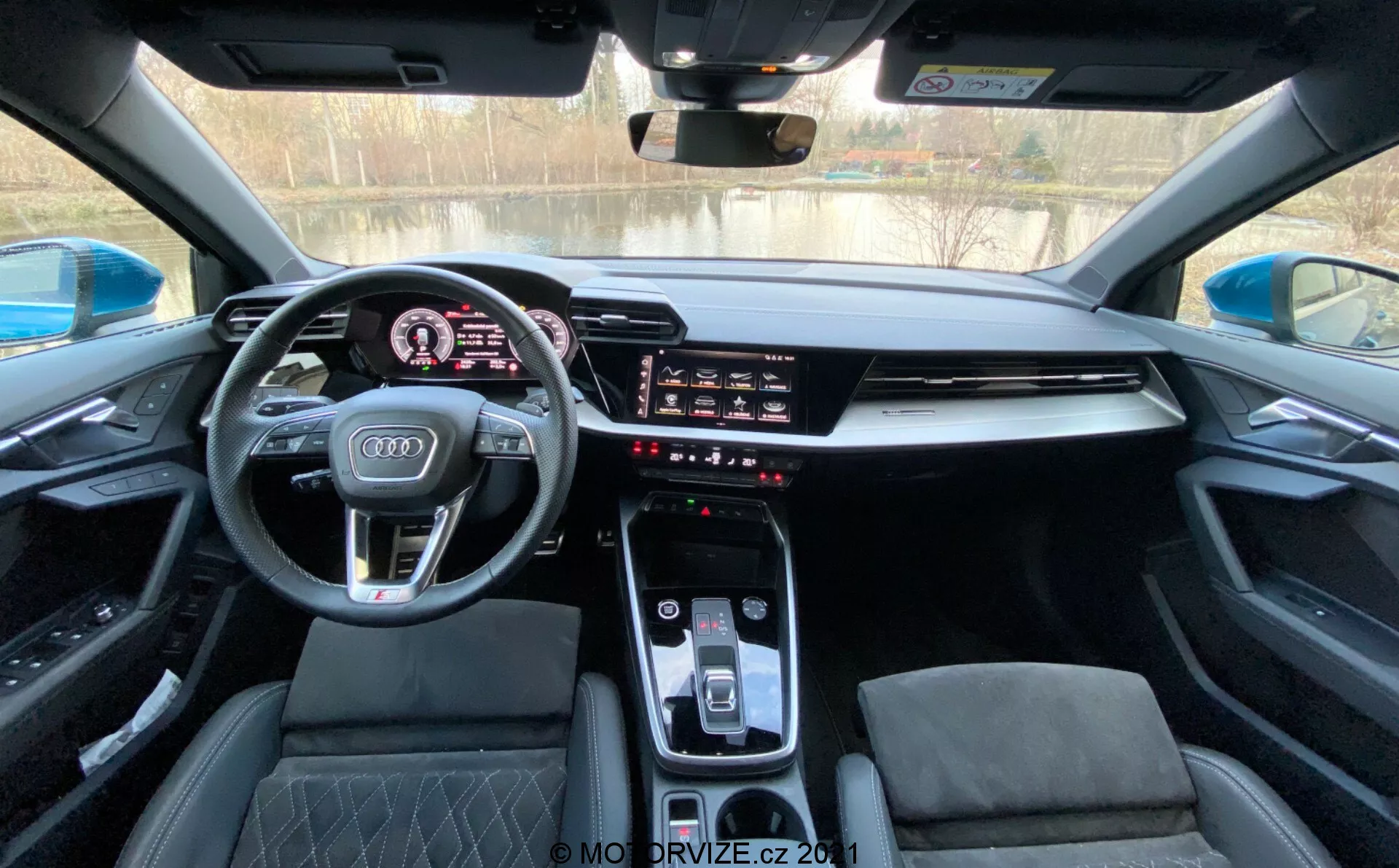 Interiér modelu Audi A3 Sportback 2020 z pohľadu vodiča, zobrazujúci modernú prístrojovú dosku s digitálnym prístrojovým panelom, športovým multifunkčným volantom s logom Audi, integrovaným infotainment dotykovým displejom, elegantným stredovým panelom s automatickým voličom prevodovky, ovládaním klimatizácie a športovými sedadlami s diamantovým prešívaním pod panoramatickým strešným oknom.