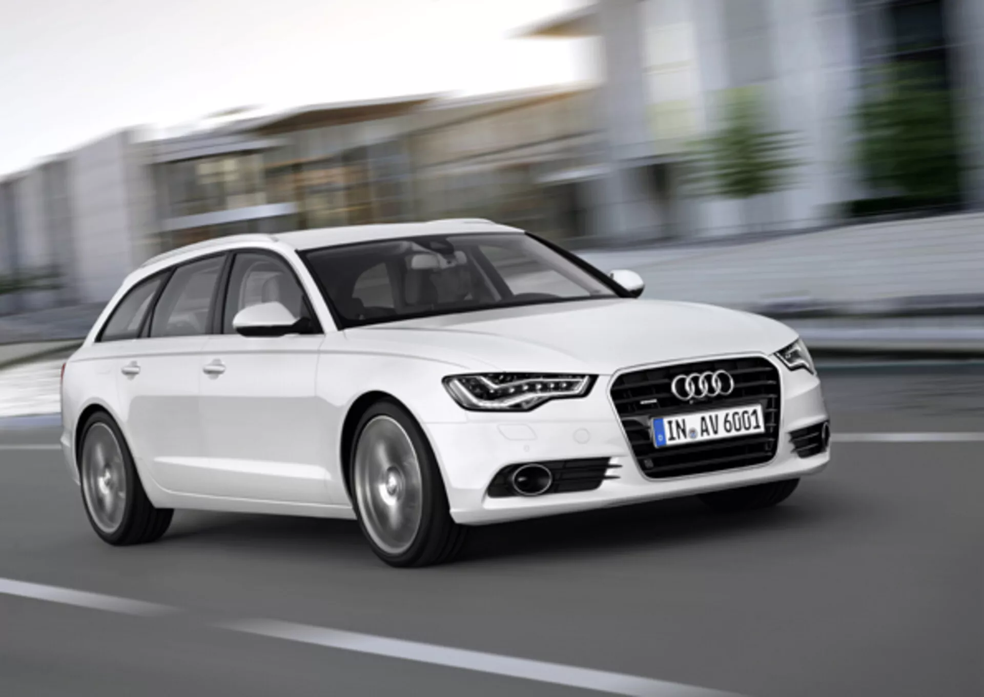 Biely Audi A6 Avant z roku 2011 v pohybe, zachytený z nízkeho uhla spredu a z boku, ktorý zdôrazňuje mriežku, LED denné svetlá, zliatinové kolesá a dynamický dizajn