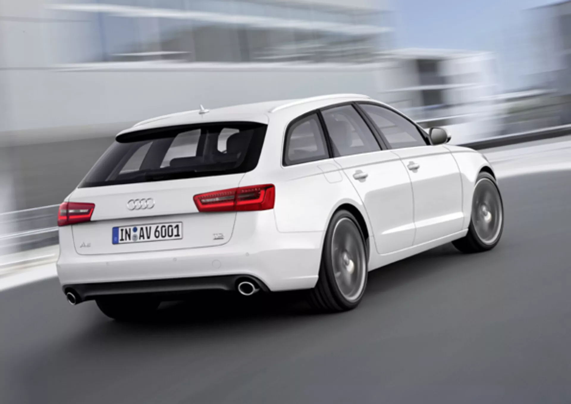 Dynamický trojštvrťový zadný pohľad na biely Audi A6 Avant z roku 2011 v pohybe, s rozmazanými kolesami naznačujúcimi rýchlosť, duálnym výfukom, zliatinovými kolesami s viditeľnými diskovými brzdami a strešným spojlerom pre lepšiu aerodynamiku, fotografované vonku.