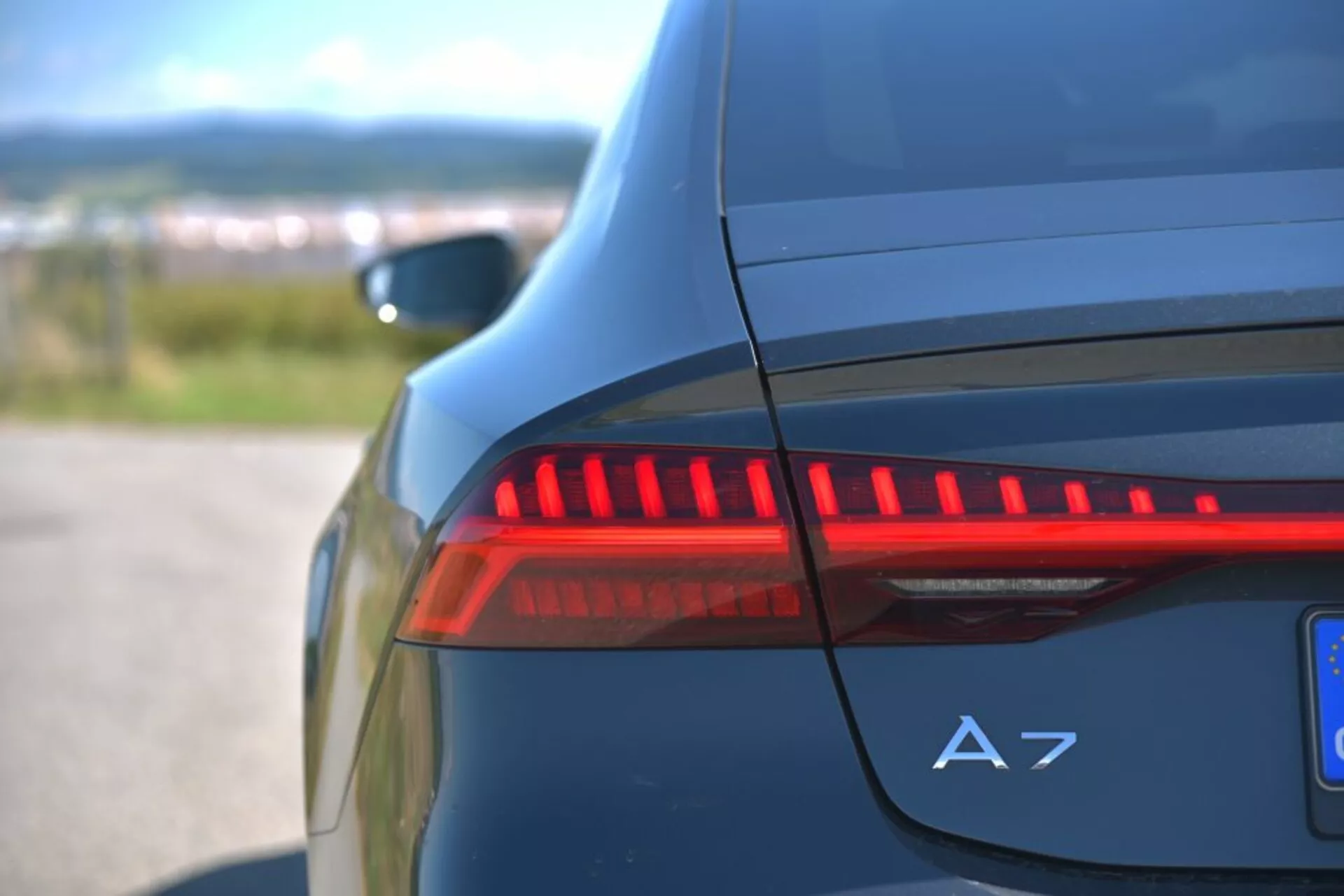 Detailný pohľad na osvetlené LED zadné svetlo a označenie A7 na zadnej strane tmavo modrého Audi A7 Sportback, zdôrazňujúci moderné prvky automobilového dizajnu a luxusné detaily