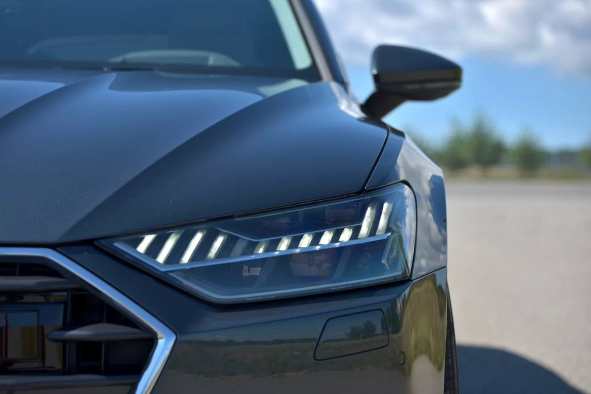 Detailný záber na Audi A7 Sportback 2018 s dôrazom na dizajn LED svetlometov, čiastočný pohľad na mriežku a aerodynamické línie z nízkeho uhla, predstavujúci moderné prvky luxusného auta a pokročilú technológiu osvetlenia
