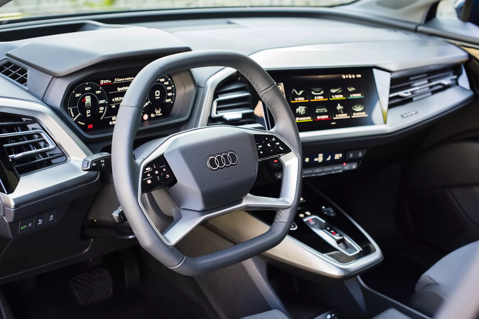 Interiér Audi Q4 e-tron 2021 z pohľadu vodiča, zobrazujúci multifunkčný volant s logom Audi, digitálny prístrojový panel, stredovú konzolu s radením, dotykové ovládacie prvky HVAC, displej infotainmentu, elegantnú palubnú dosku s integrovanými ventiláciami a luxusne čalúnené dvere z kože, ukazujúci modernú technológiu automobilov a funkcie luxusných vozidiel.