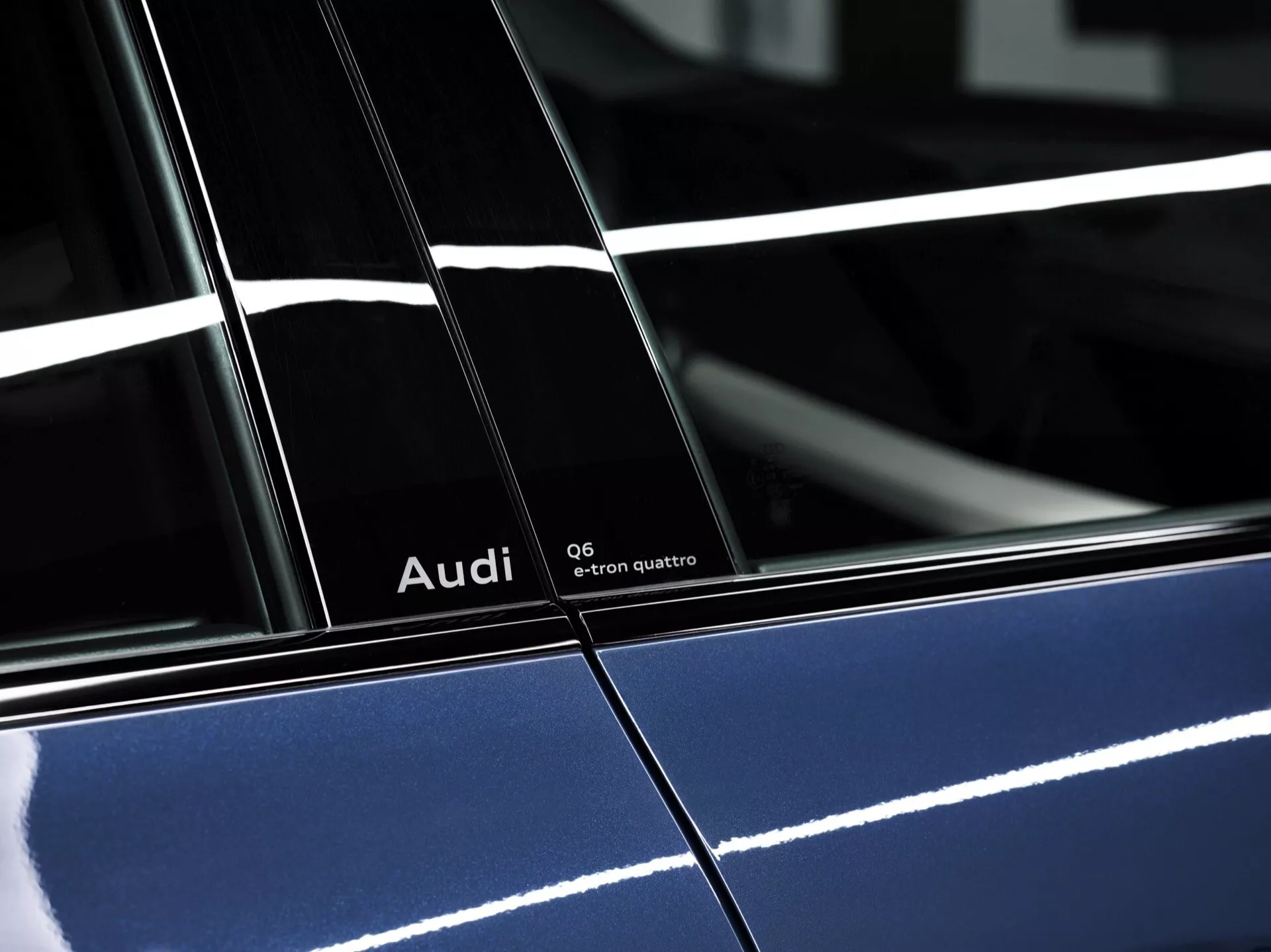 Vysokokvalitný bočný profil 2024 Audi Q6-e-tron quattro v hlbokej modrej farbe s lesklým povrchom, zobrazujúci výrazné označenie a detaily dizajnu, zdôrazňujúci B-stĺpik medzi dverami a odrazy osvetlenia.