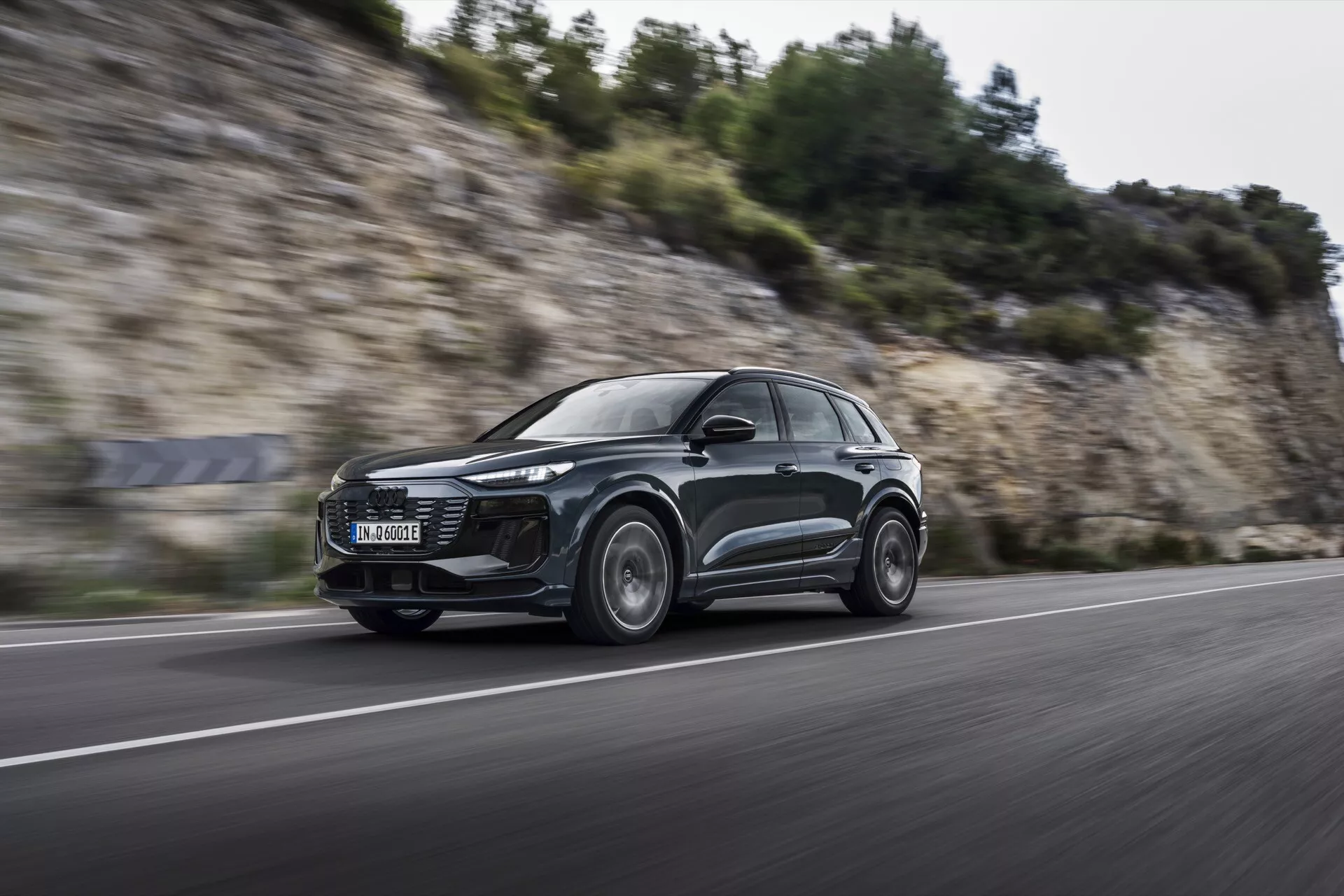 Dynamický záber Audi Q6 e-tron 2024 v pohybe z nízkeho, čelného uhla, zobrazujúci jeho elegantný aerodynamický dizajn SUV, moderné LED svetlomety a zliatinové kolesá s rozmazaním pohybu, naznačujúci výkonnostné schopnosti na asfaltovej ceste.