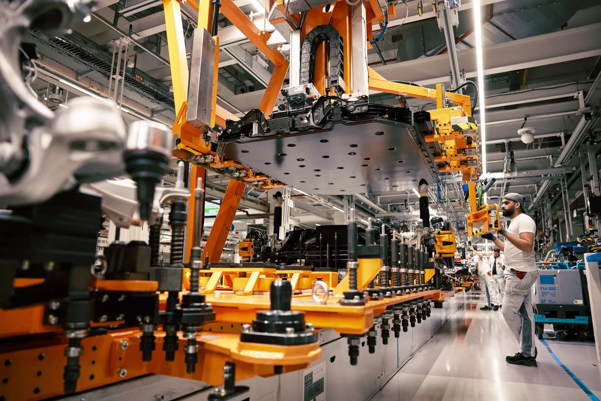 Montáž Audi Q8 e-tron 2023 v priemyselnom závode, zobrazujúca robotickú ruku manipulujúcu s karosériou vozidla bez dverí alebo kolies na montážnej linke