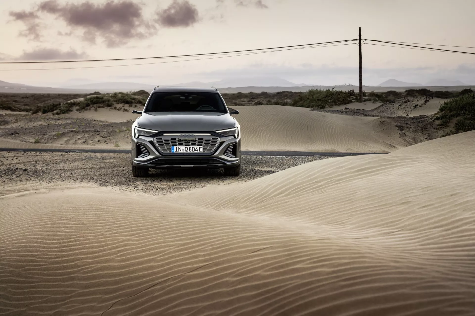 Čelný pohľad na Audi Q8 e-tron 2023 v krajine púšte pri svitaní alebo súmraku, zdôrazňujúci jeho mriežku, kapotu a pokročilý dizajn svetlometov