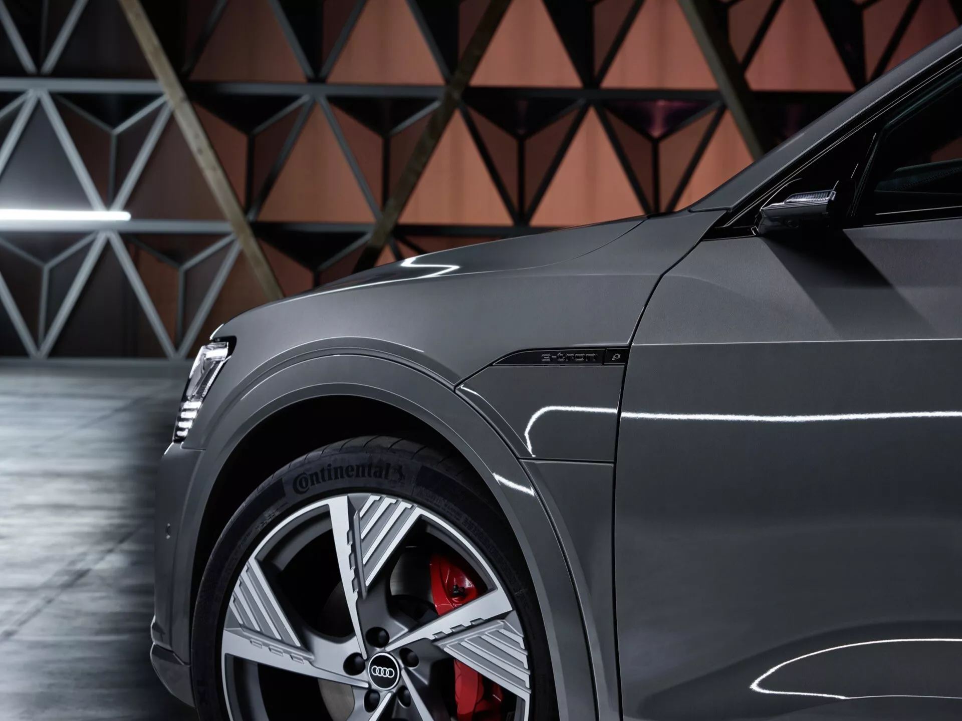 Detailný bočný pohľad na Audi Q8 e-tron 2023 zameraný na predný štvrťový panel, ukazujúci viacspojkové zliatinové koleso, vysokovýkonnú pneumatiku Continental, červený brzdový strmeň s veľkým diskom a lesklý lak s športovými dizajnovými čiarami