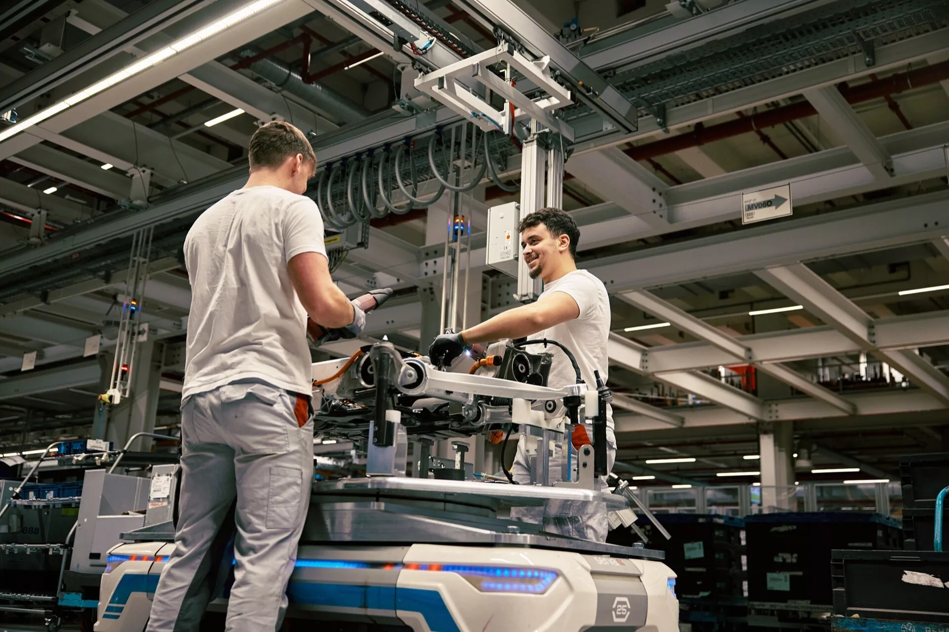 Priemyselné prostredie s dvoma pracovníkmi montujúcimi alebo udržiavajúcimi mechanické zariadenia na podlahe továrne, pod umelým osvetlením, s výhľadom zvýšeného hľadiska zdôrazňujúcim výrobné prostredie