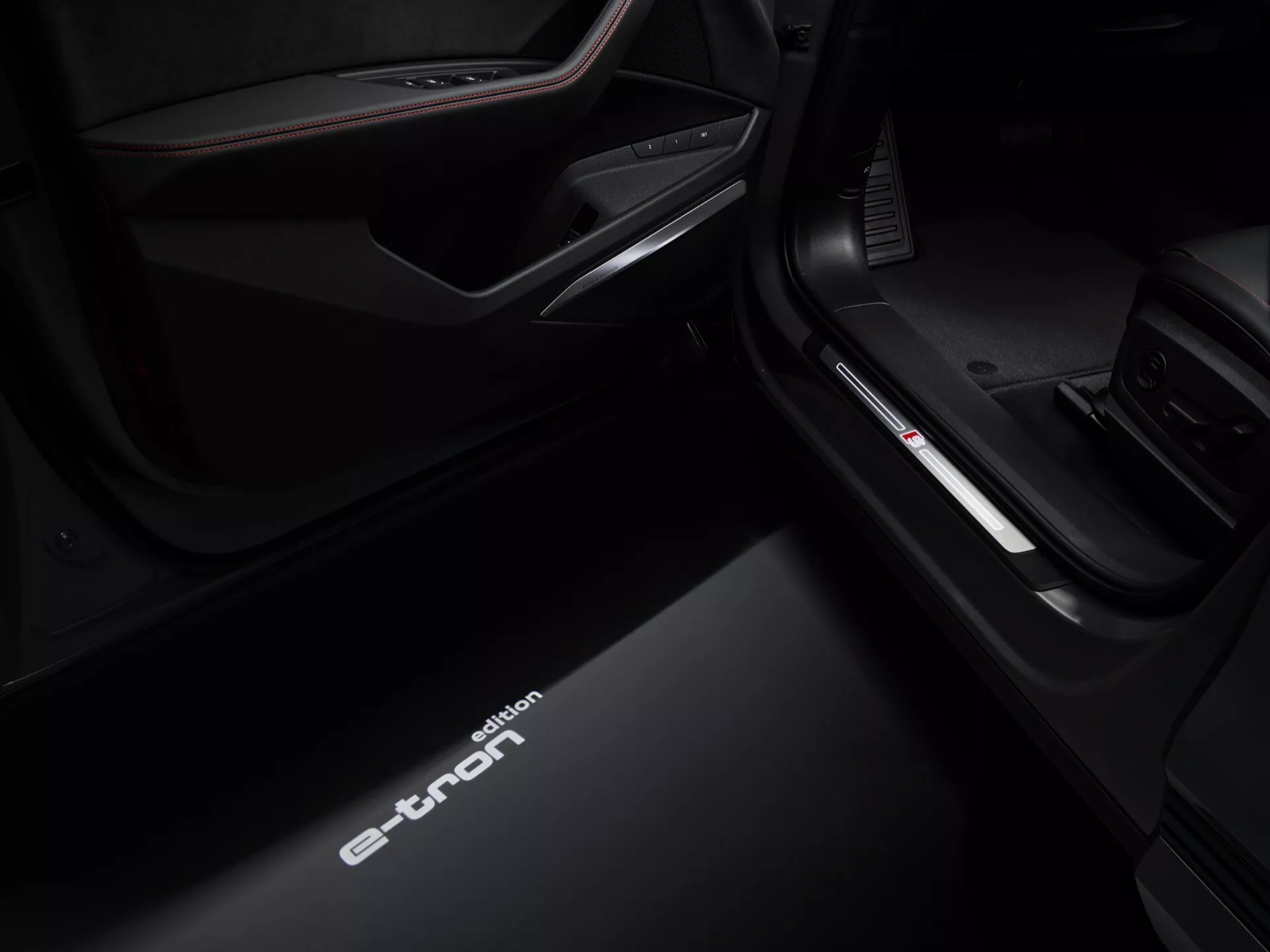 Pohľad z nízkeho uhla na prah dverí na strane spolujazdca interiéru Audi Q8 e-tron 2023, predvádzajúci osvetlený nápis 'e-tron', zdokonalené interiérové osvetlenie a detaily prémiovej výbavy
