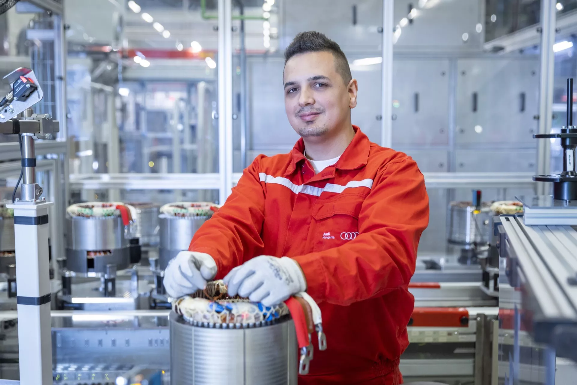 Odborník na automobilové inžinierstvo v červenej uniforme pracuje na komponente elektrického pohonu v modernej výrobnej závode