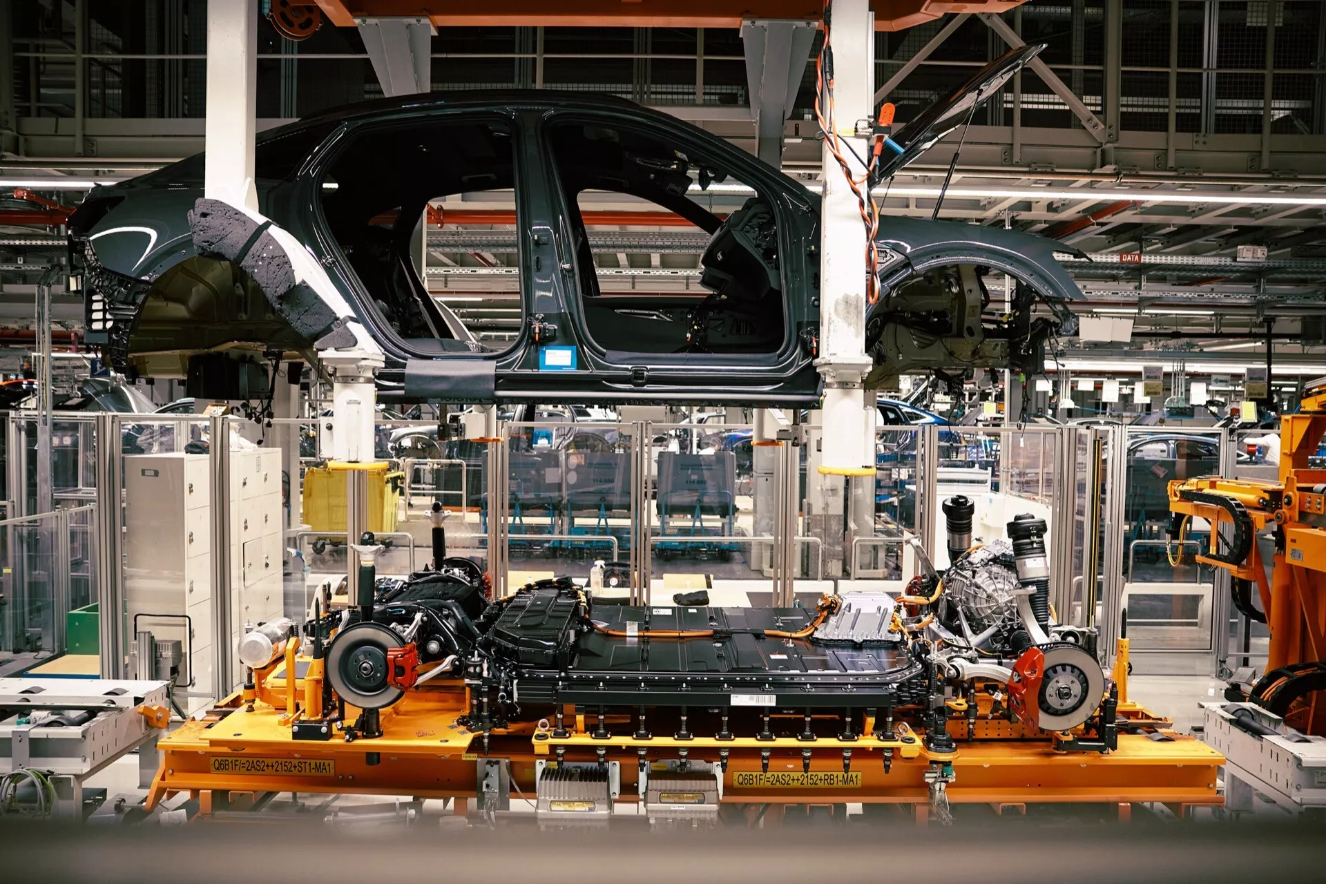 Čiastočne zostavené Audi Q8 e-tron 2023 na výrobnej linke, ukazujúce podvozok a inštaláciu motora v automobilovom závode
