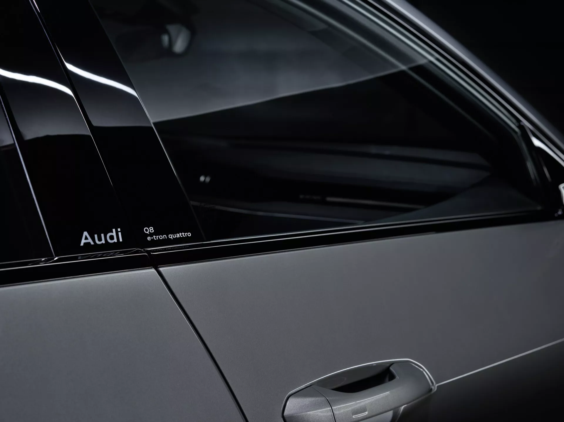 Detail bočného profilu Audi Q8-e-tron 2023 s odznakom Quattro, stĺpikom C a zadným oknom pre cestujúcich, zdôrazňujúci dizajn vozidla a systém pohonu všetkých kolies