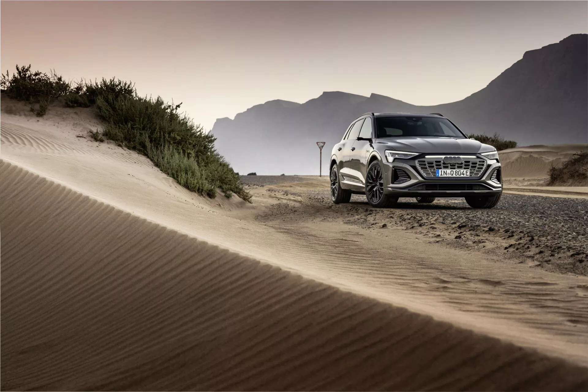 Audi Q8 e-tron 2023 v teréne predvádzajúce luxusný SUV dizajn, LED svetlomety, zliatinové kolesá a výkonnostné schopnosti na pozadí piesočných dún počas zlatej hodiny
