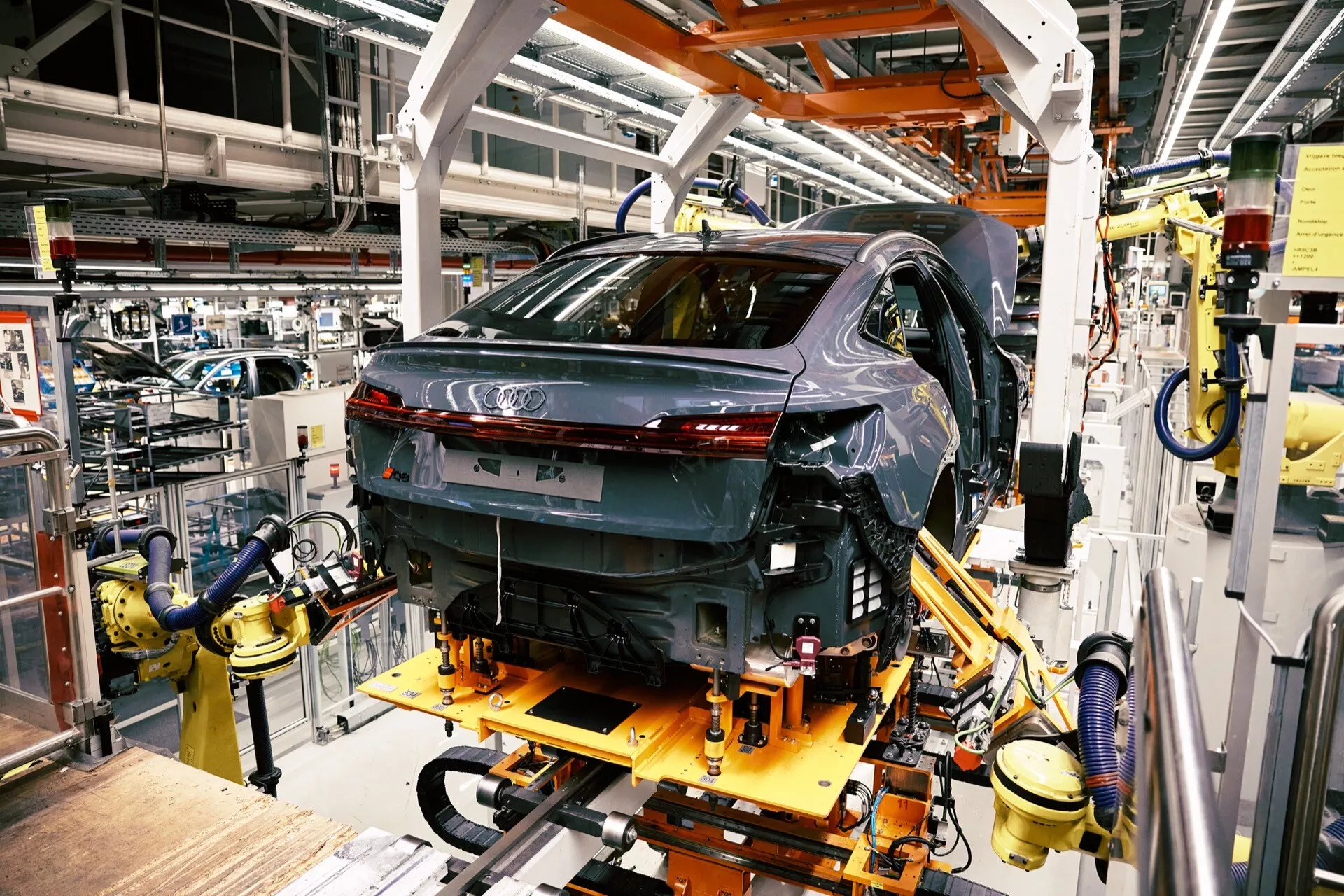 Audi Q8 e-tron 2023 vo výrobe, pohľad z zadnej trojštvrte pozície ukazujúci LED zadné svetlá a vysoko lesklý povrch na montážnej linke