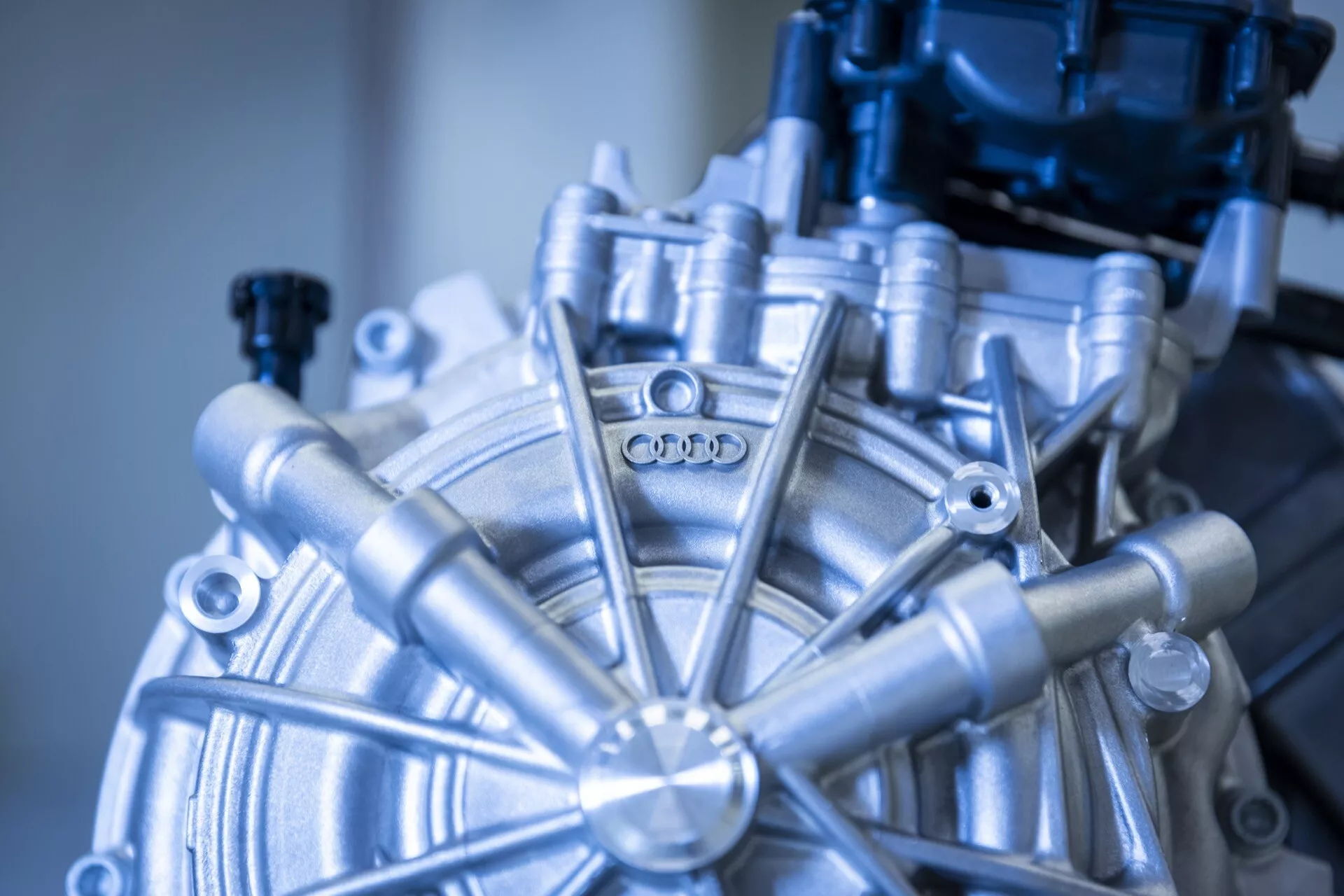Detailný pohľad na súčiastku motora Audi Q8 e-tron 2023, ktorá zobrazuje kruhové centrum s vyžarujúcimi prvkami a logom Audi, predvádzajúcu pokročilé automobilové inžinierstvo a presnú výrobu.