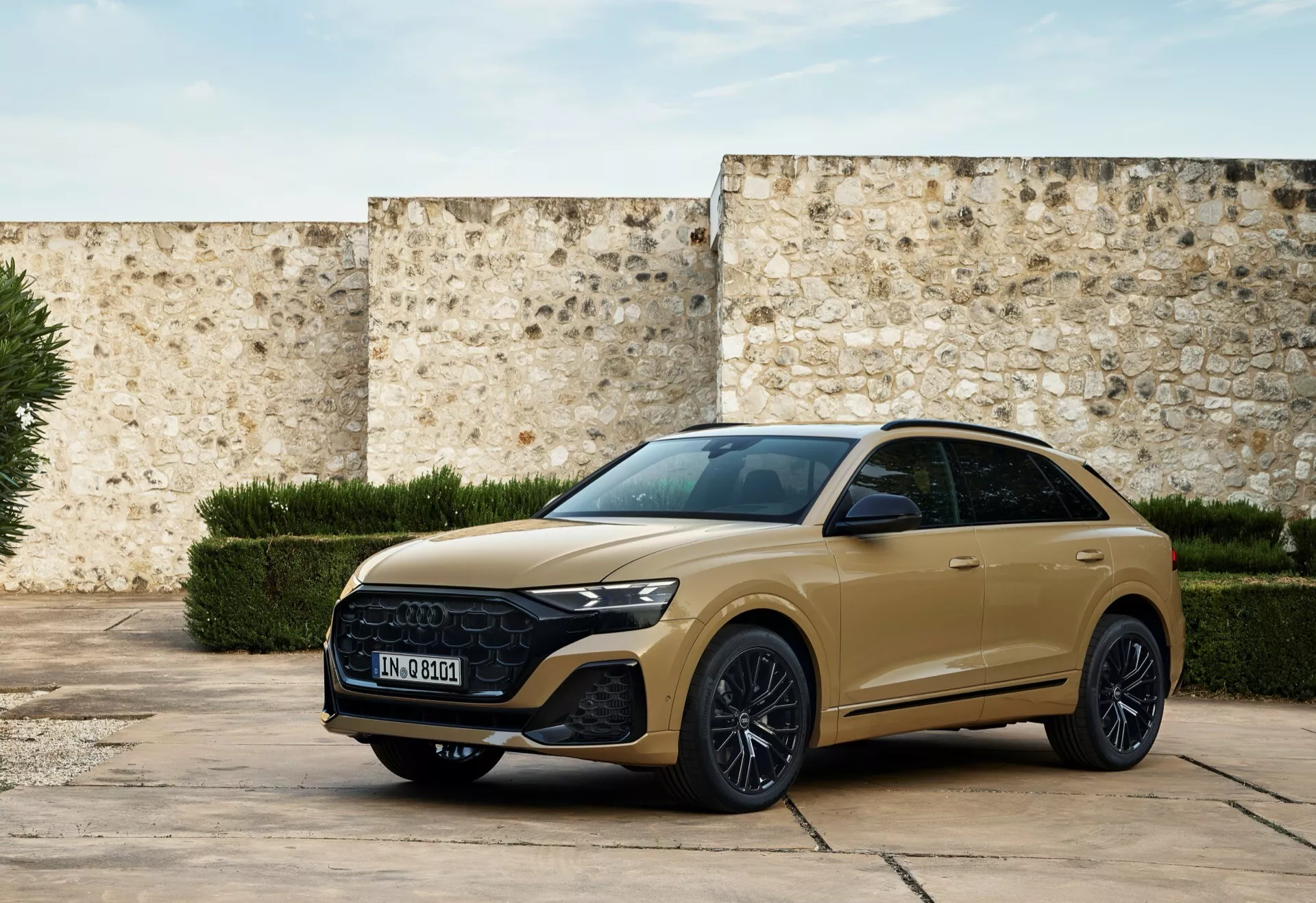 Moderné SUV Audi Q8 2023 (4M-Facelift) v tlmenom zlate, zaparkované na historickom nádvorí prezentujúce prednú mriežku, štýlové svetlomety a športový bočný profil s technologickými funkciami a prvkami luxusného dizajnu pri prirodzenom svetle