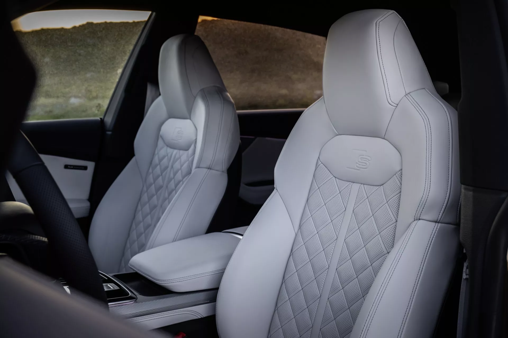 Interiér Audi Q8 2023 (4M-Facelift) s dôrazom na luxusné predné sedadlá so svetlou diamantovou čalúnením a vytlačeným logom Mercedes-Benz, s náhľadom na vysokotechnologickú konzolu v strede z pozície mimo stredu vzadu.