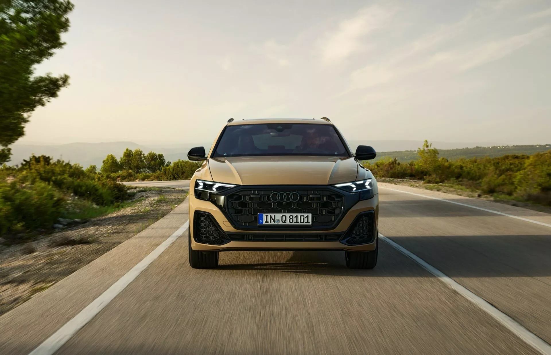 Čelný pohľad na moderné auto jazdiace po otvorenej ceste skoro ráno alebo neskoro popoludní, predvádzajúce elegantné LED svetlomety, výraznú mriežku a náznaky pokročilých asistenčných systémov vodiča
