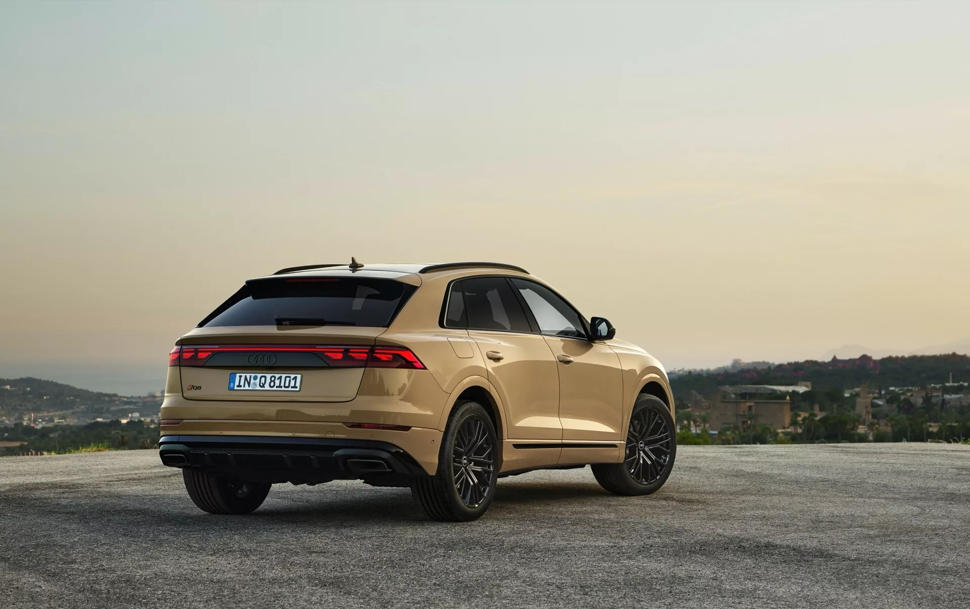 Audi Q8 2023 (4M-Facelift) s metalickým povrchom, zaparkované na vyhliadkovom mieste s kopci a oblohou na úsvit/západ slnka, ukazujúce uhla zadných troch štvrtín pre pohľad na dizajn a funkcie