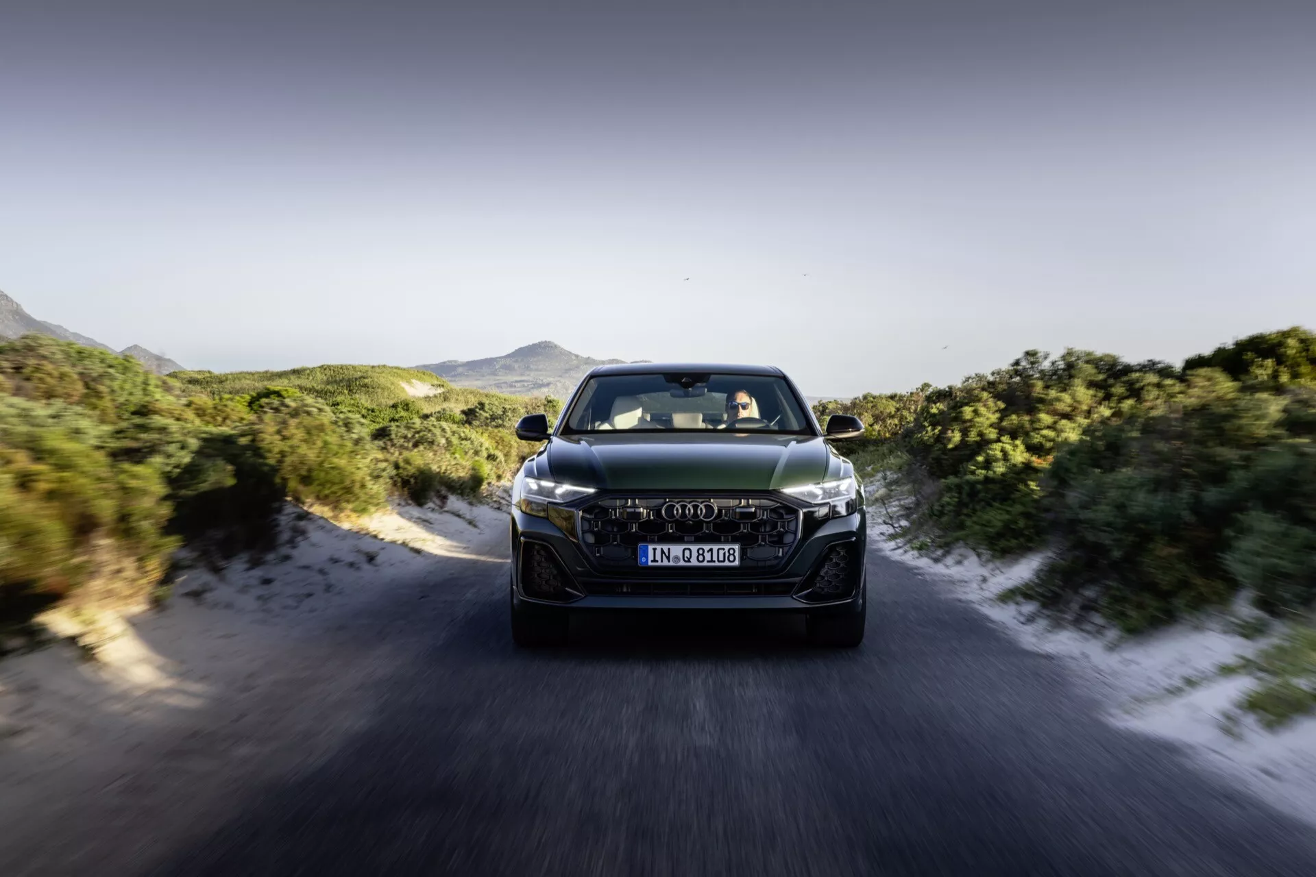Audi Q8 4M-Facelift 2023 v pohybe, čelný pohľad ukazujúci LED svetlomety, pokročilý dizajn mriežky a aerodynamické prvky proti dynamickému pozadiu cesty a hôr
