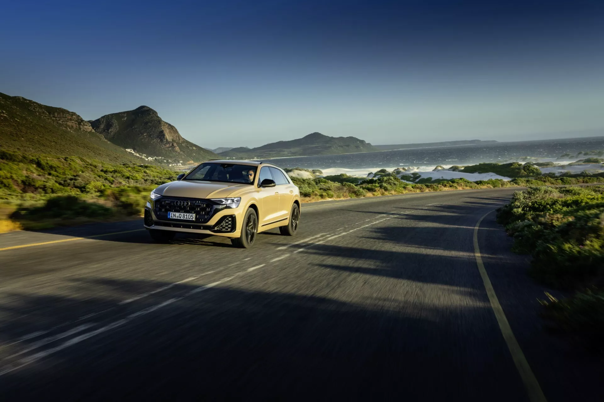 Audi Q8 2023 (4M-Facelift) idúce pozdĺž pobrežnej cesty, predvádzajúce svoj dynamický dizajn a LED svetlomety v trojštvrťovom prednom pohľade s rozostrením pohybu