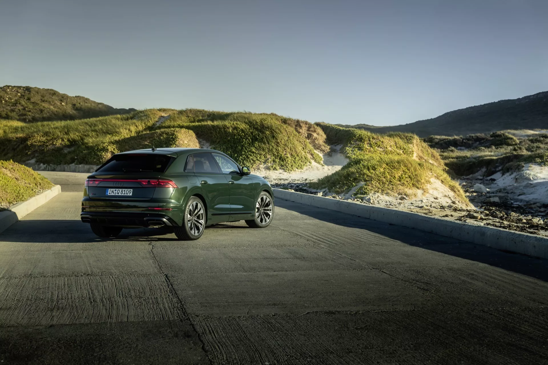 Audi Q8 4M-Facelift 2023 predstavené proti pobrežnej dunajskej krajine počas zlatej hodiny, ukazujúce zadný trojštvrtečný pohľad s modernými vodorovnými zadnými svetlami a elegantným dizajnom