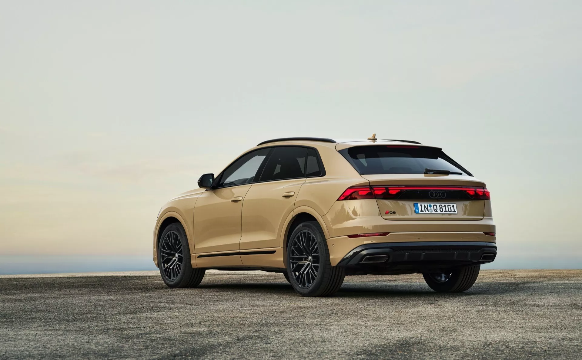 Zadný trojštvrťový pohľad na Audi Q8 4M facelift 2023 na betóne pod oblohou na svitaní alebo súmraku zdôrazňujúci LED zadné svetlá, zliatinové kolesá, spoiler na streche, panoramatické strešné okno a dvojité výfukové výstupy