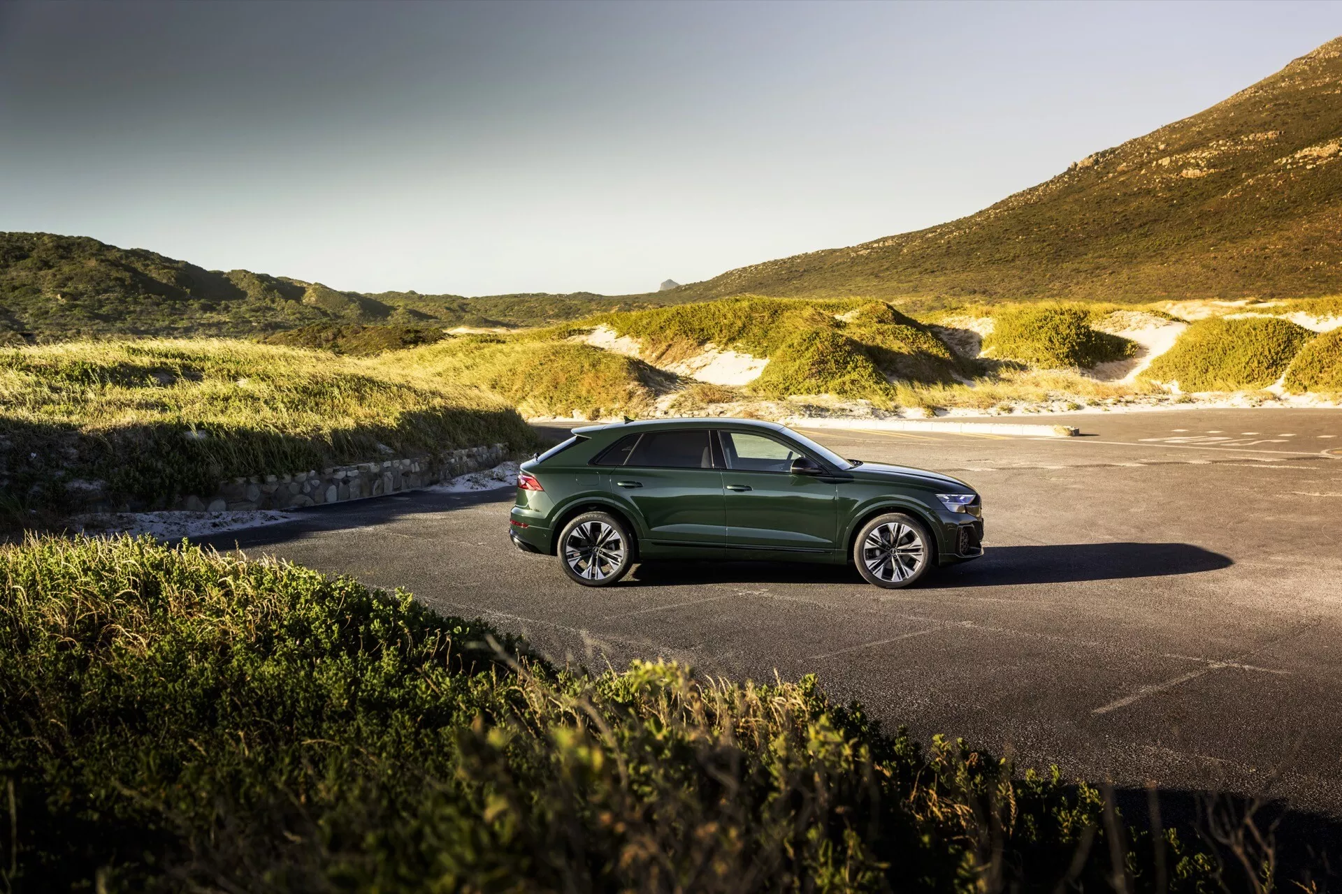 Audi Q8 2023 (4M-Facelift) v zelenej farbe zaparkované s pôsobivým prírodným pozadím, možno pobrežným alebo horským, pod jasnou oblohou