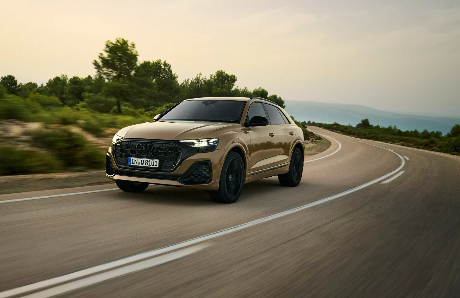 Audi Q8 2023 (model 4M facelift) zachytené v dynamickej jazdnej scéne, zamerané na jeho aerodynamickú prednú mriežku, LED svetlomety a štíhly profil z nízkeho uhla predných troch štvrtín naznačujúci rýchlosť a prémiové funkcie