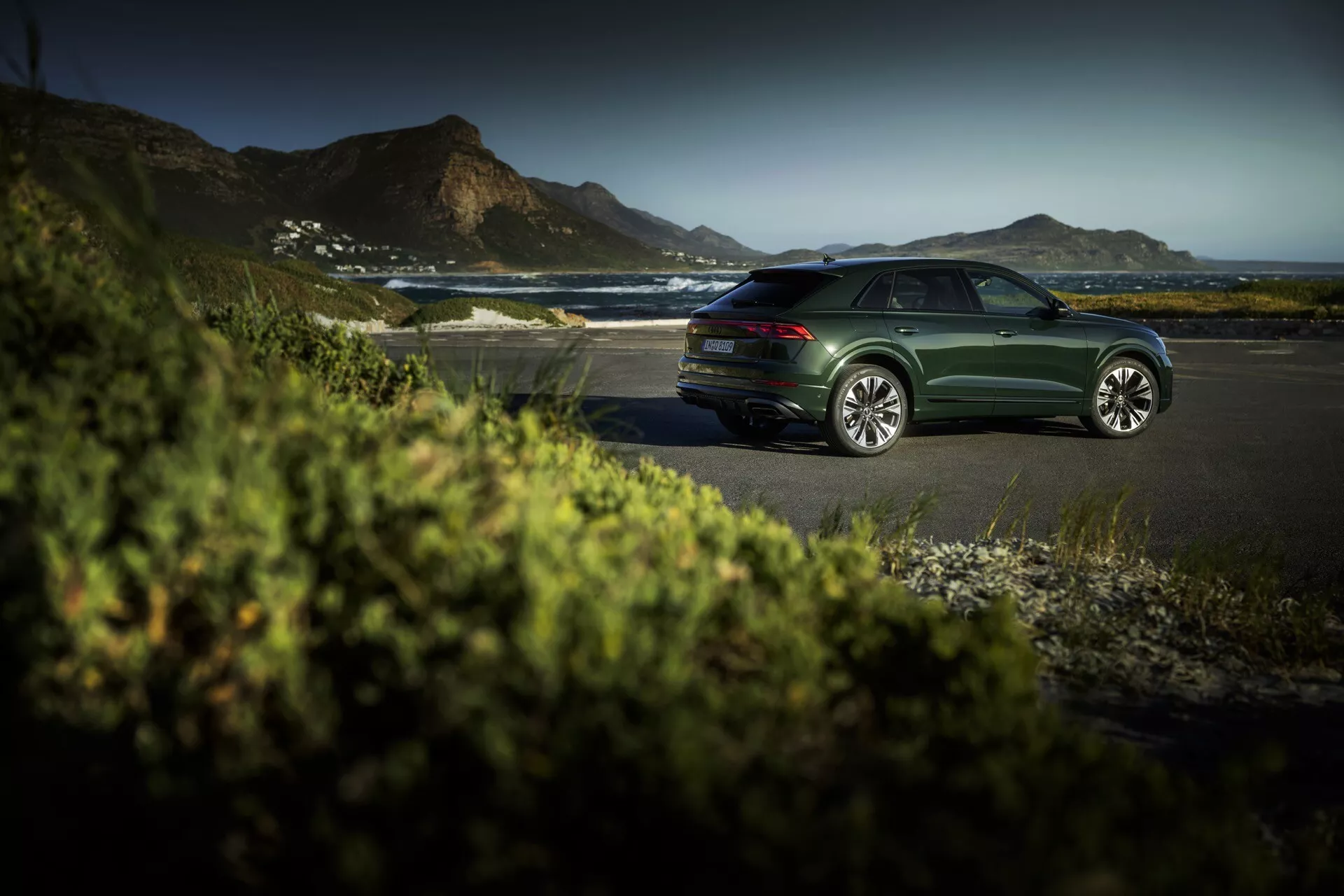 Sedan Audi Q8 (4M-Facelift) tmavo zelenej farby zaparkovaný na pobrežnej ceste počas zlaté hodiny, ukazujúci elegantné dizajnové línie, viacramenné zliatinové kolesá a pokojné luxusné vonkajšie prostredie