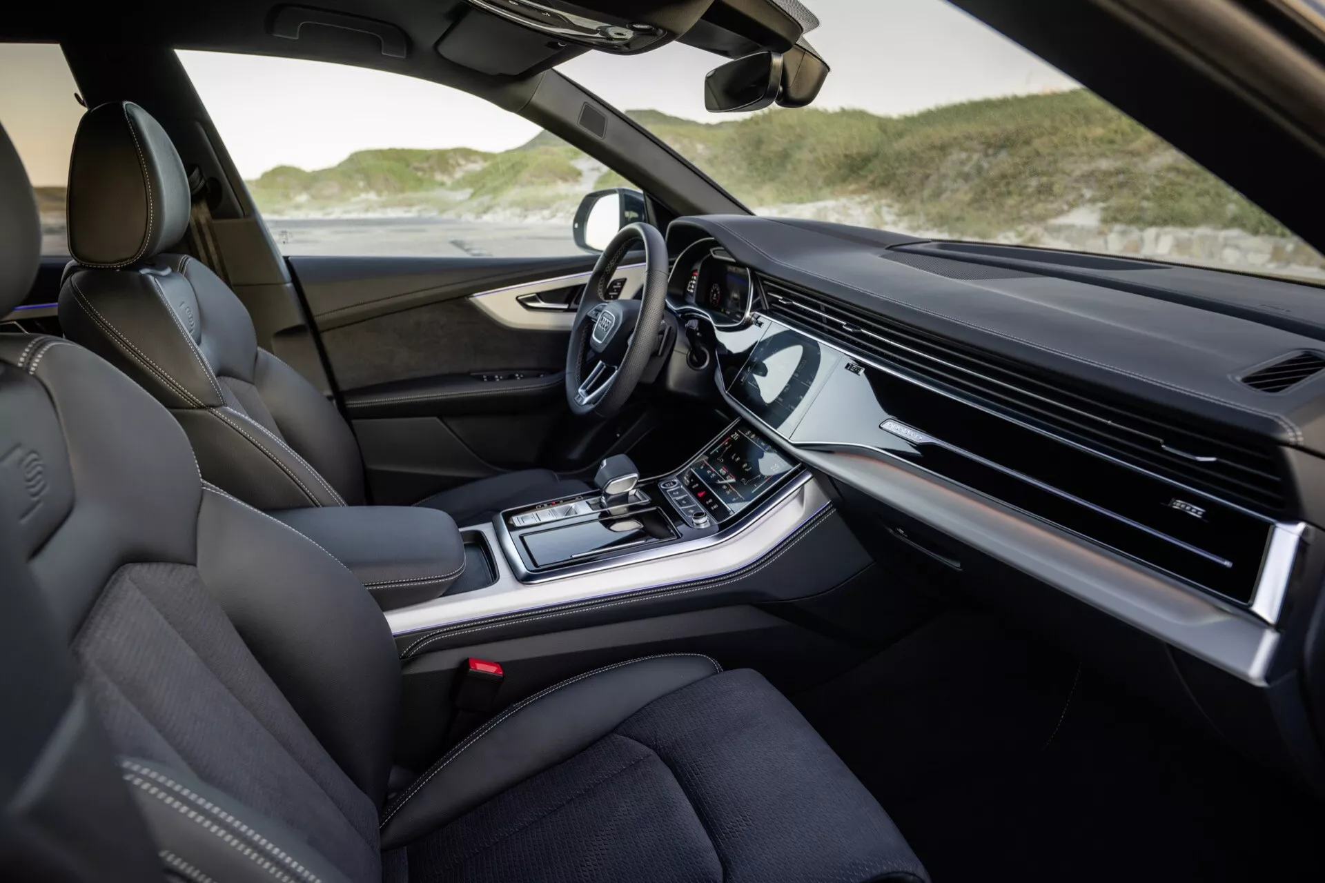 Interiér Audi Q8 2023 (4M-Facelift) z pohľadu spolujazdca s luxusnými koženými sedadlami, pokročilým palubným panelom s integrovaným displejom infotainment, stredovou konzolou s ovládaním klímy a režimu jazdy, modernou automatickou radicou pákou a volantom vybaveným technológiami