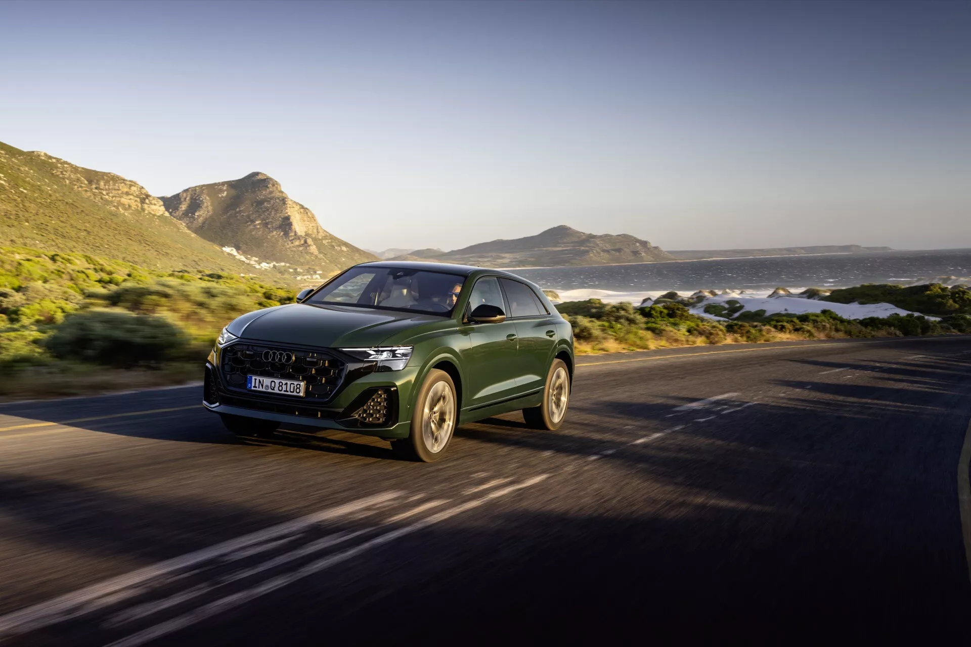 Audi Q8 4M-Facelift 2023 idúce po pobrežnej ceste, zvýraznené svojím aerodynamickým dizajnom, LED svetlometmi a emblémom výrobcu na mriežke, zachytené z uhla tri štvrtiny zpredu, predvádzajúce luxusné SUV v pohybe proti malebnému pozadiu